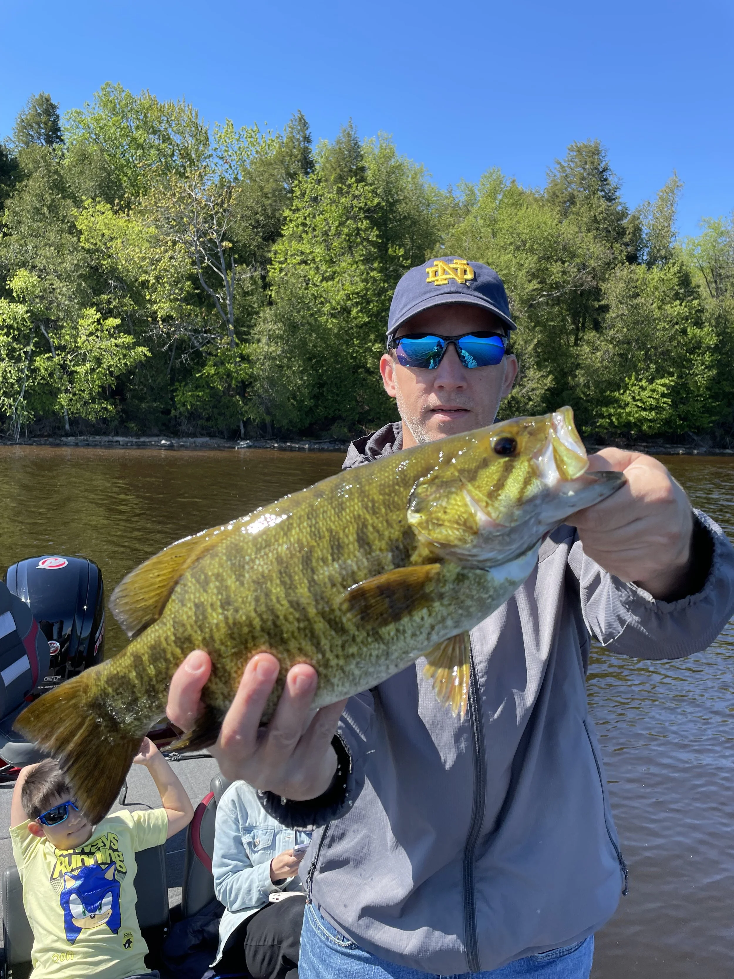 Man holding a fish on a boat with forest background