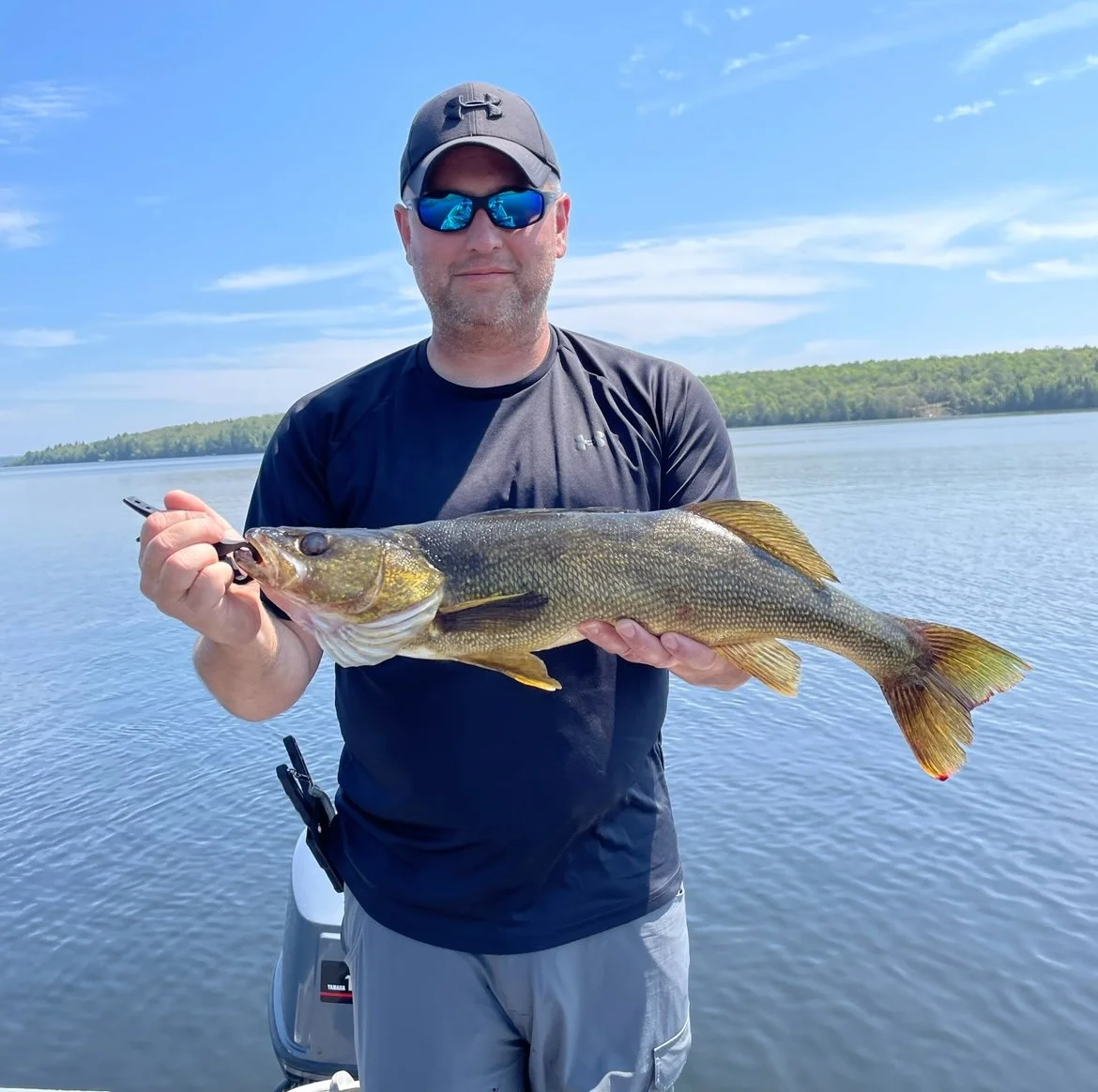 Bass Fishing Guide Services - Fishing Guide - Twin Lakes, MI - Person holding a large fish on a boat with a lake and trees in the background.