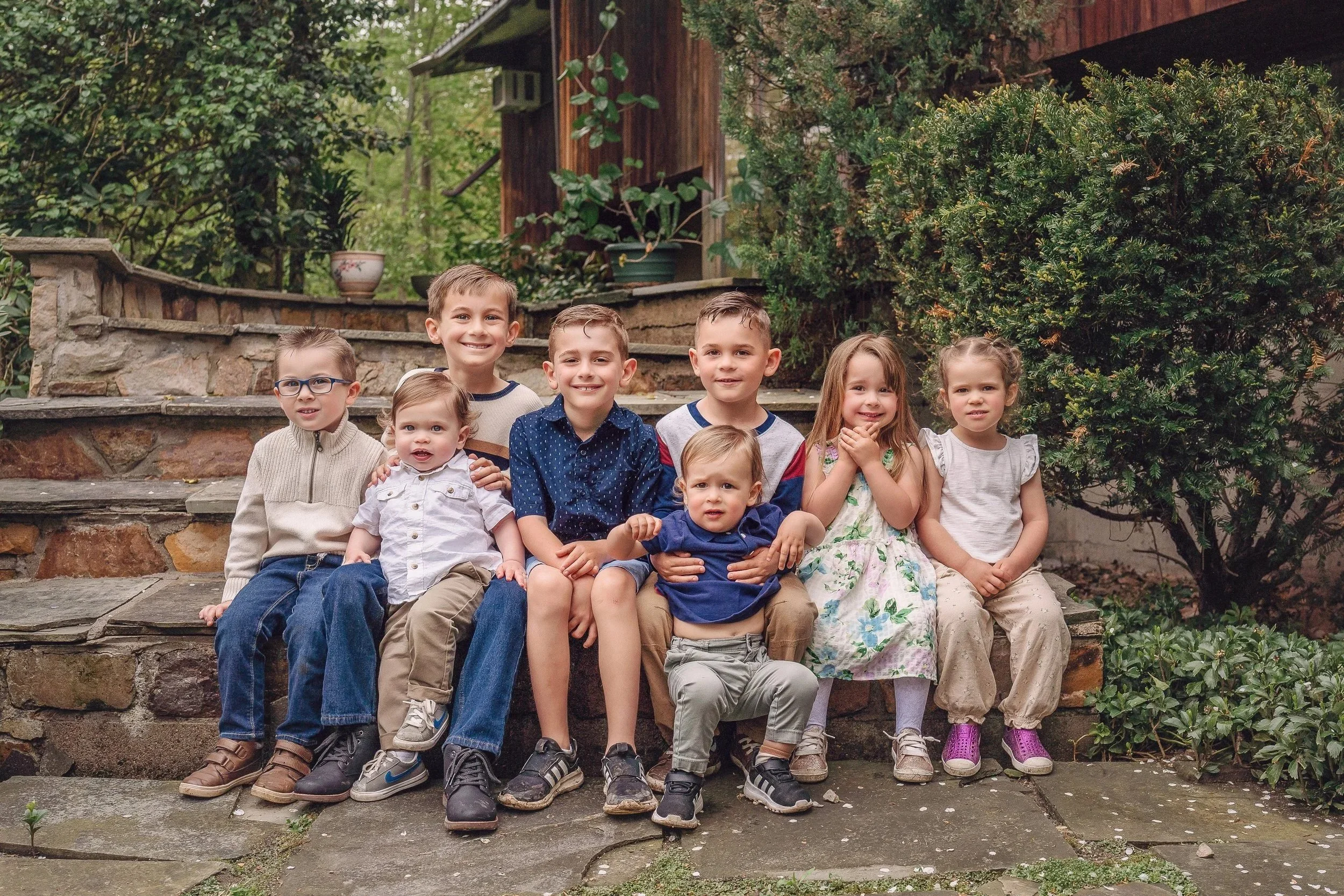 Group of 8 grandkids in various ages. sitting on rock steps with plants around them.