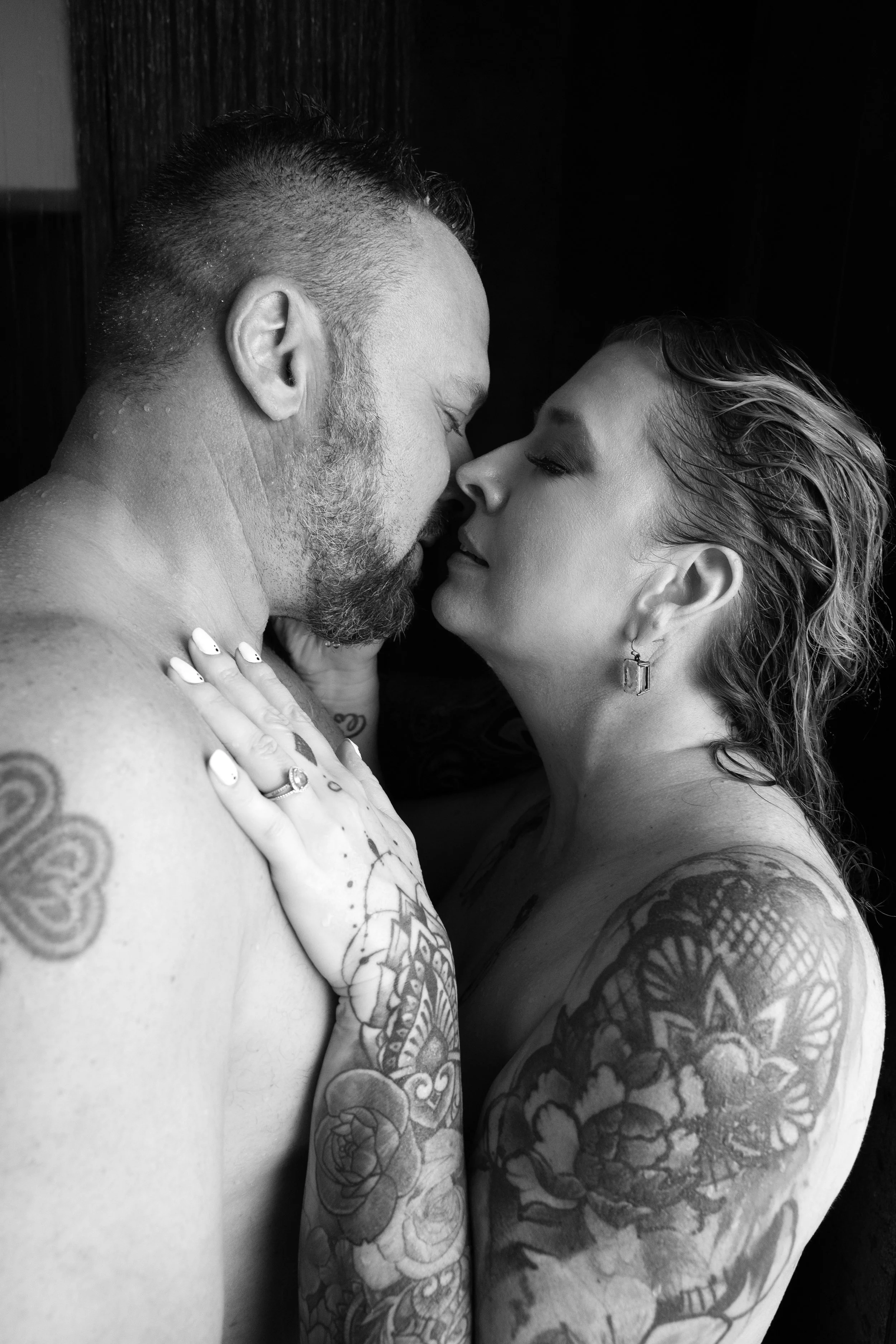 Artistic black and white image of tattooed couple sharing intimate moment in shower