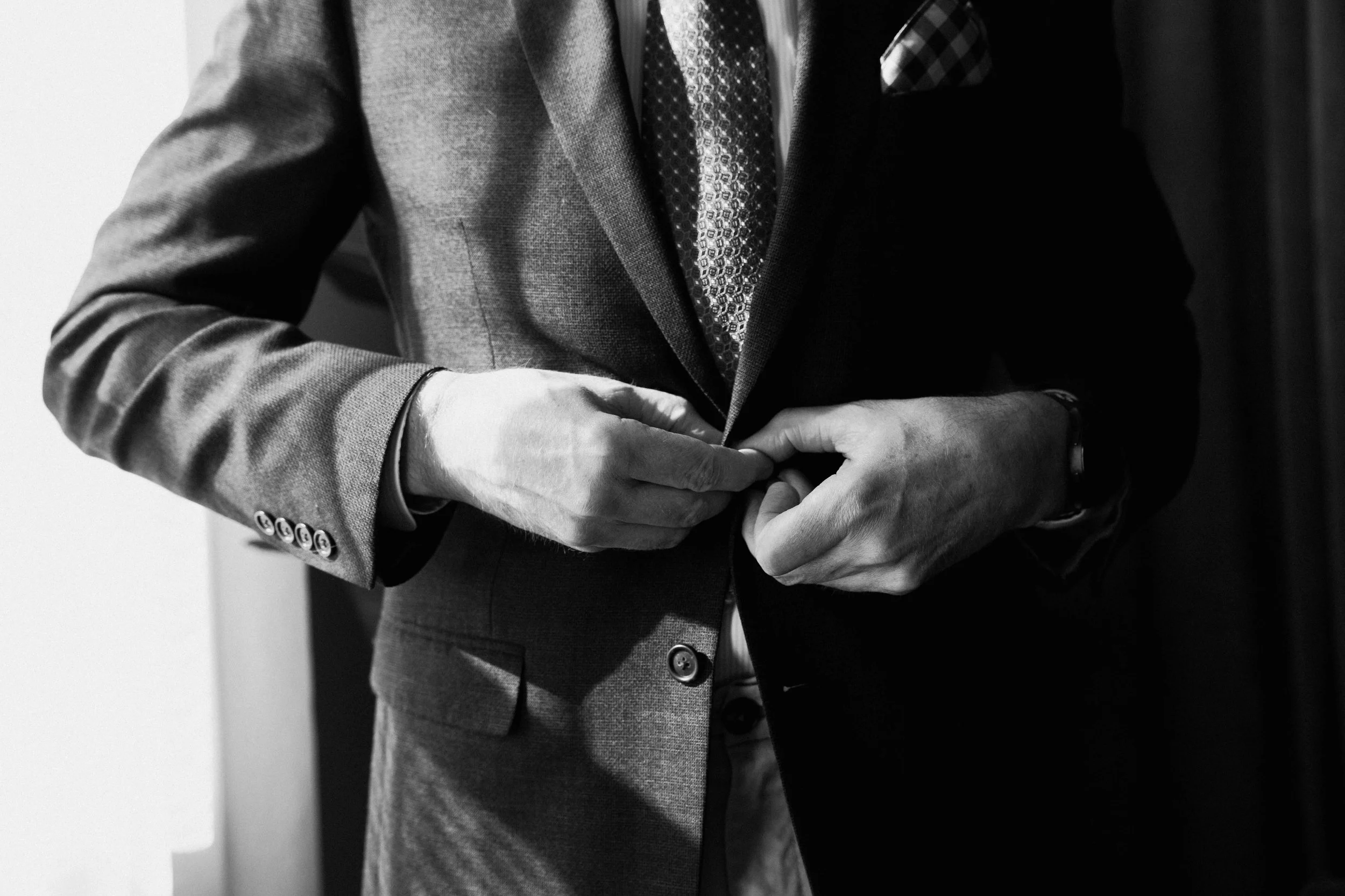 Man unbuttoning suit jacket in front of window during men’s boudoir session