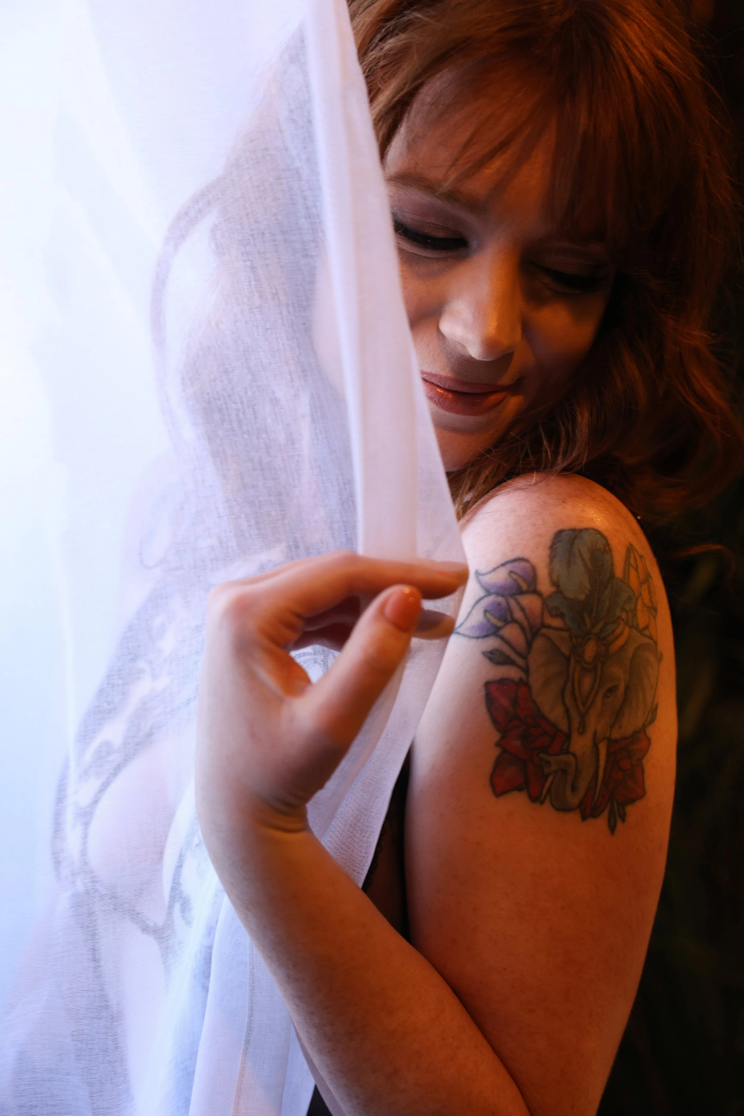 Woman standing in natural window light holding a sheer curtain during a Scottsdale boudoir session