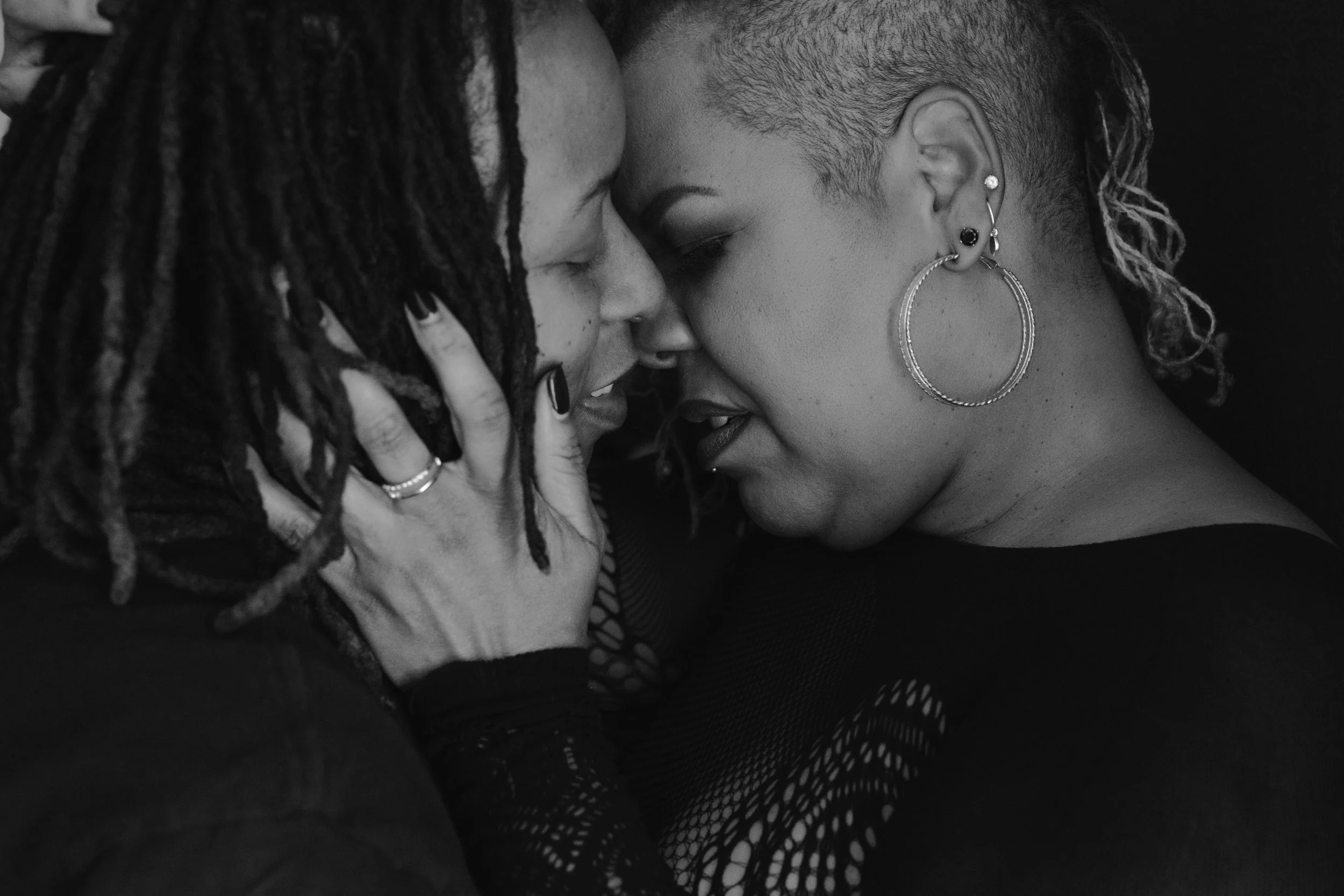 Artistic black and white portrait of two women embracing closely, captured just before a kiss