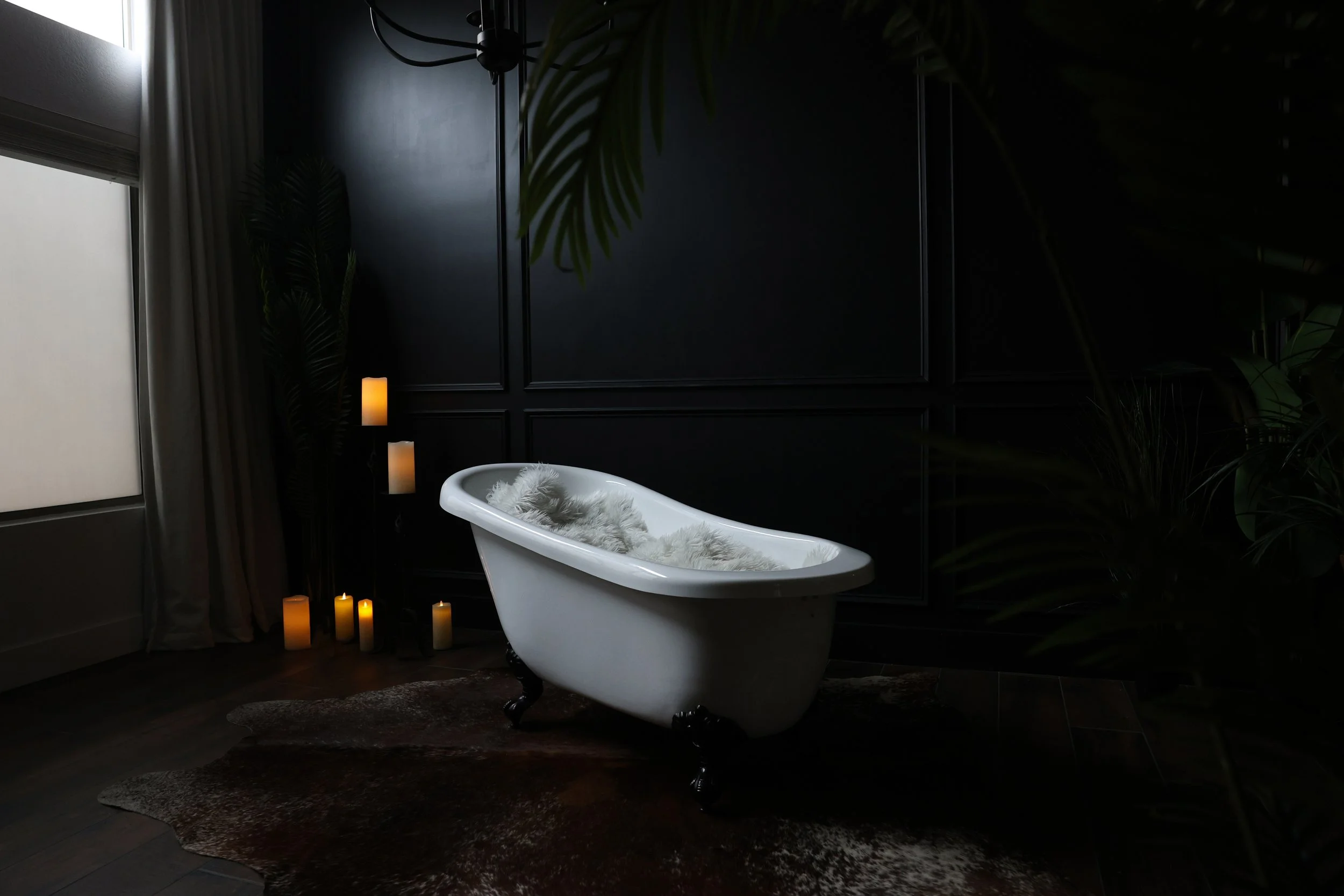 Antique clawfoot tub set with candles against black-trimmed wall and large window in boudoir studio