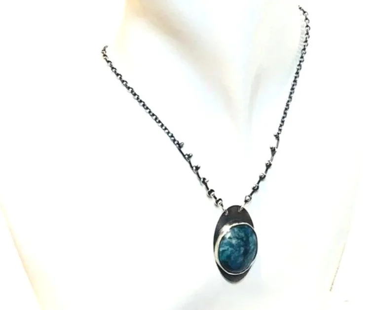 Sterling silver necklace with an oval chrysocolla stone set in a darkened silver bezel, suspended from a beaded oxidized silver chain.