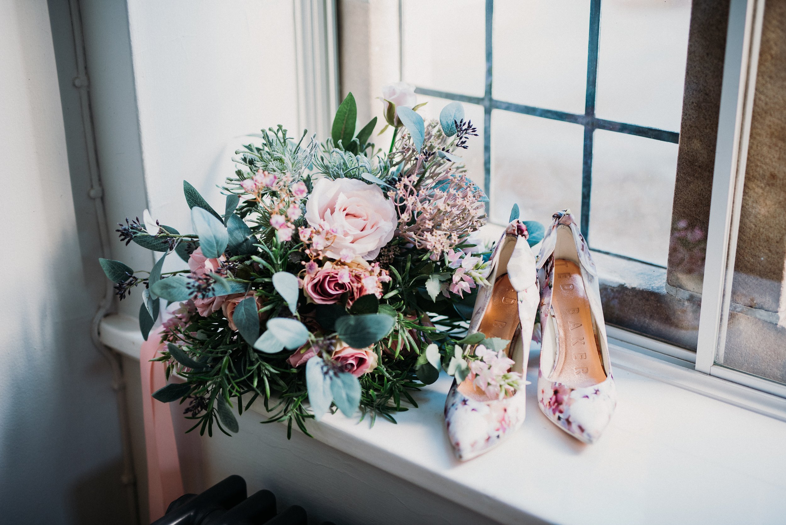 The bride's shoes and bouquet sit on a window sill in the natural light at Sneaton Castle, Whitby.