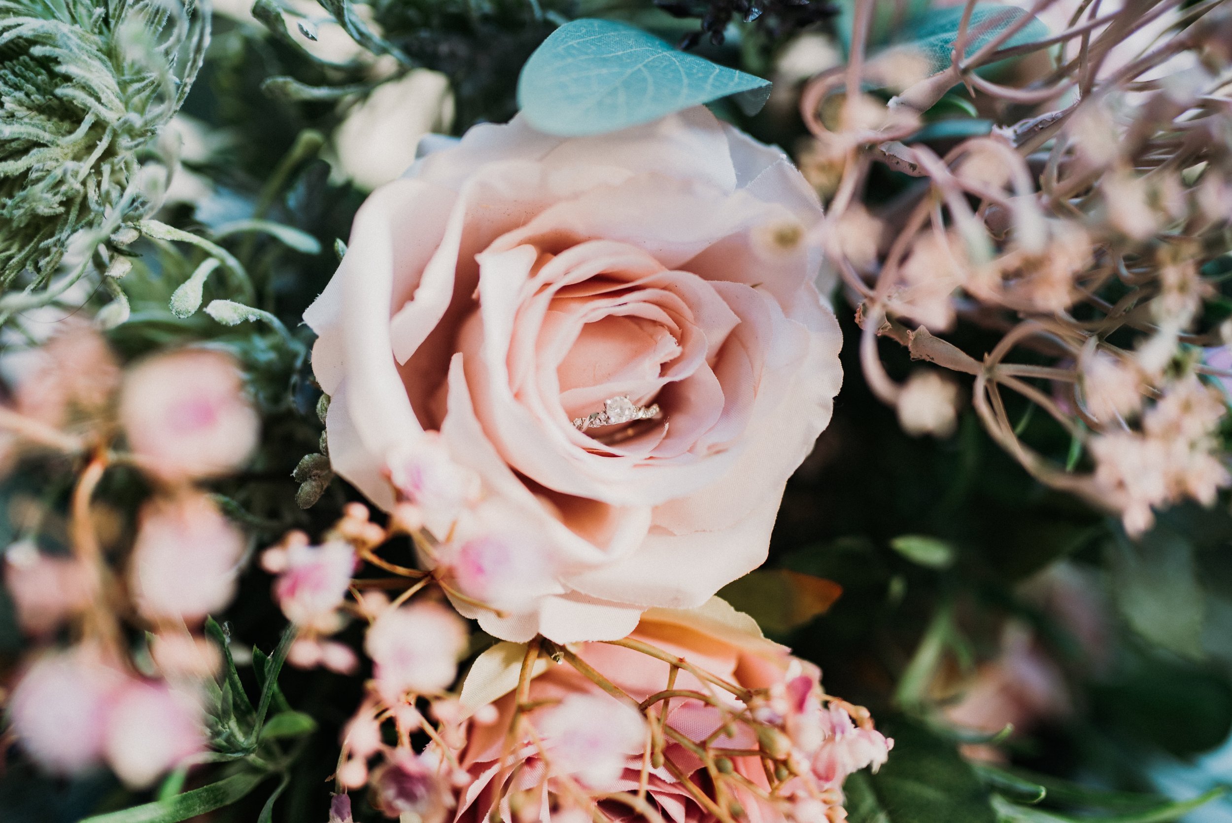 The bride's engagement ring is nestled in the petals of a pink rose in her bridal bouquet.