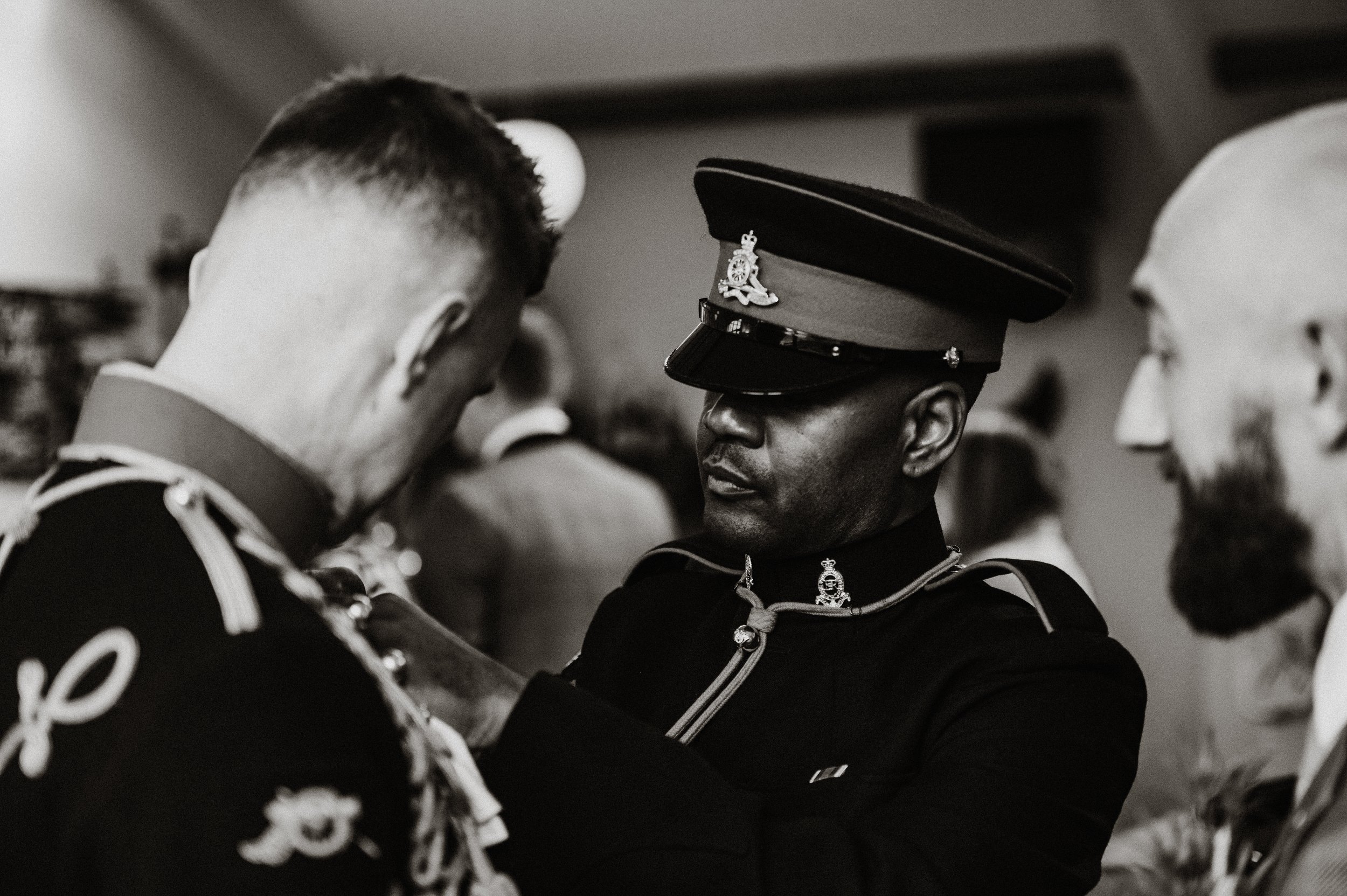 The groom is given some expert assistance with his button hole by a master tailor in full uniform.