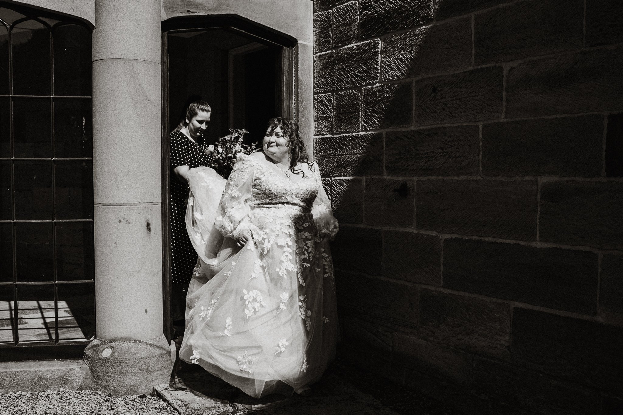 A black and white photograph of the bride leaving the bridal preparation room and heading to the ceremony room at Sneaton Castle, Whitby.