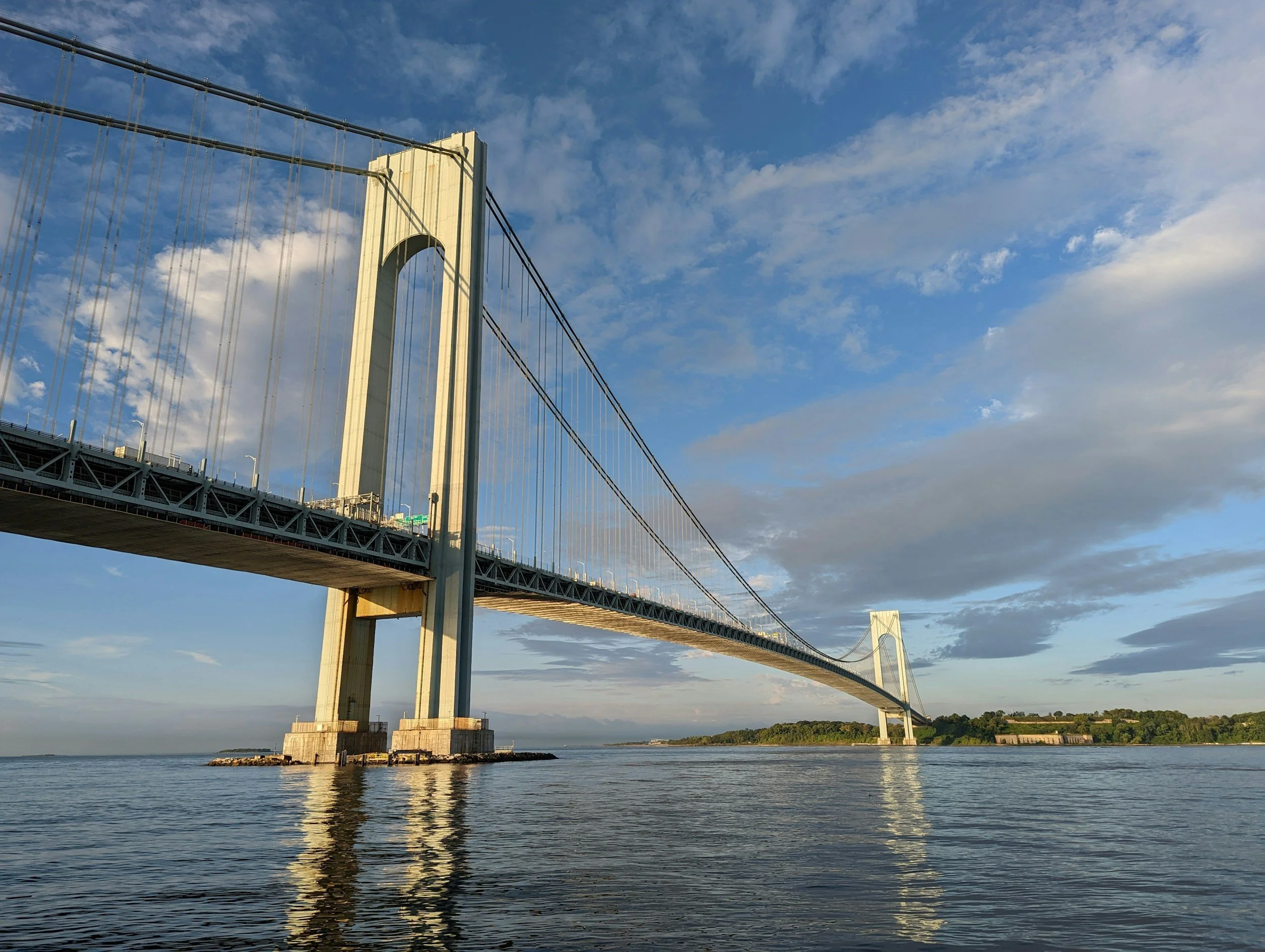 A large suspension bridge spanning over a body of water with a blue sky and some clouds above.