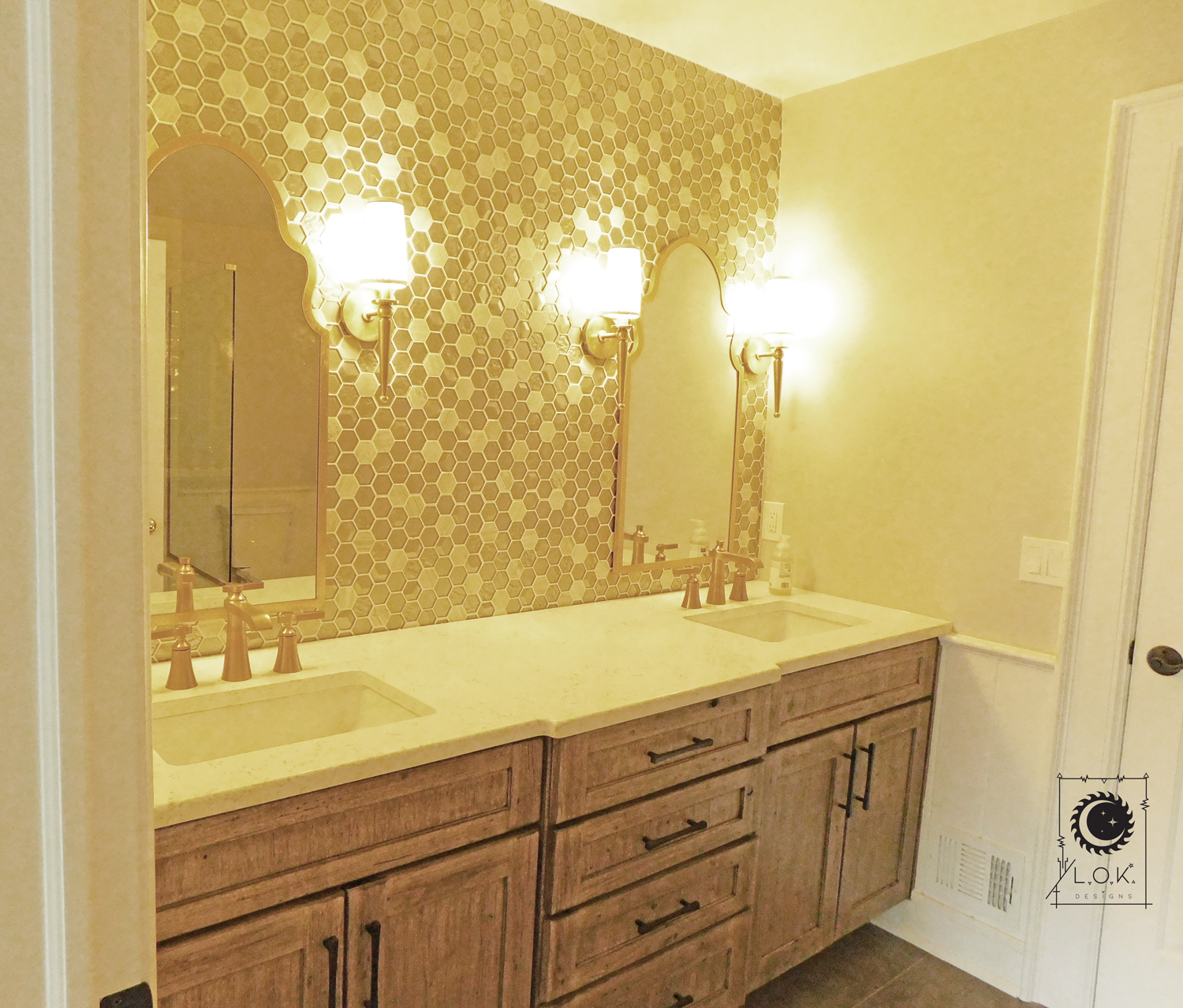 The newly renovated bathroom in Central Jersey Area now boasts a custom wood vanity with white stone countertops and oil-rubbed brass fixtures. Custom-shaped arch top mirrors, small octagon tiles in white and beige tones, and black hardware enhance t