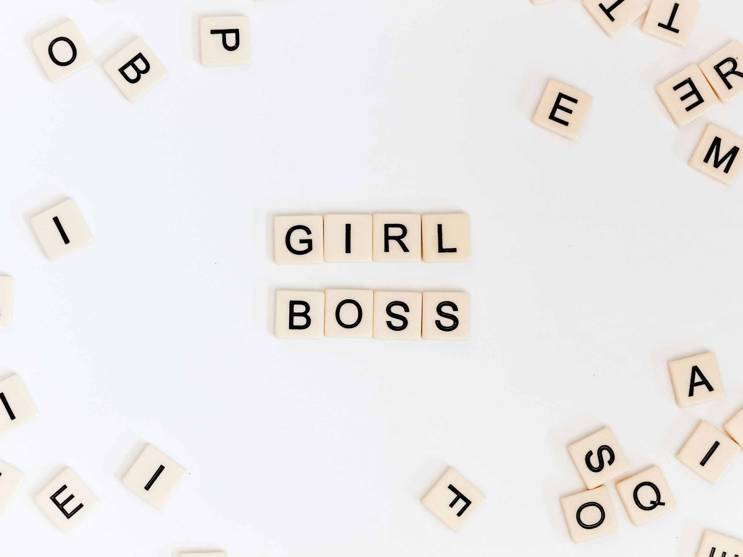 Scrabble tiles spelling out 'GIRL BOSS' on a white background among scattered tiles.