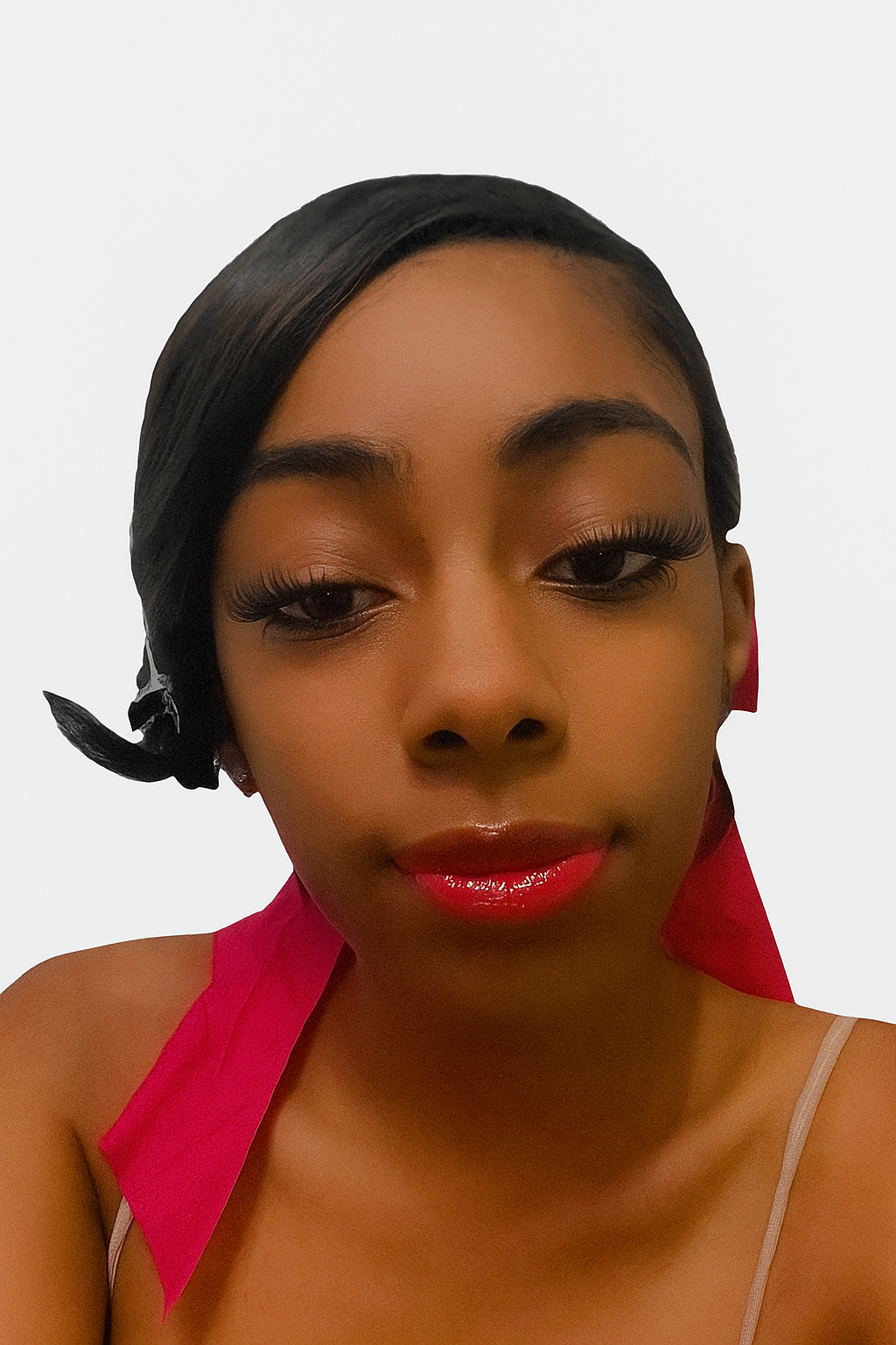 A close-up of a woman with dark hair, wearing makeup with shiny red lipstick and long eyelashes, against a plain white background.