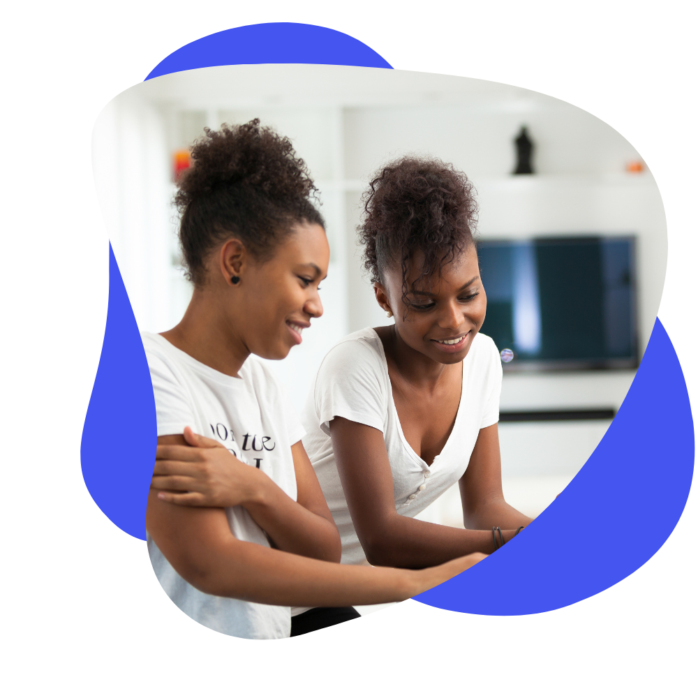 Two women with curly hair smiling and looking at a tablet in a bright room