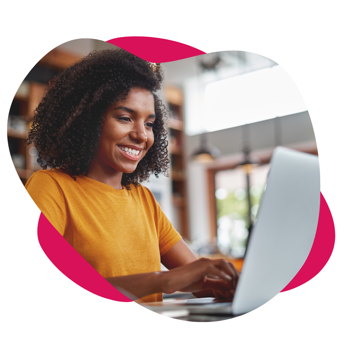 Woman with curly hair smiling while using a laptop in a well-lit cafe.