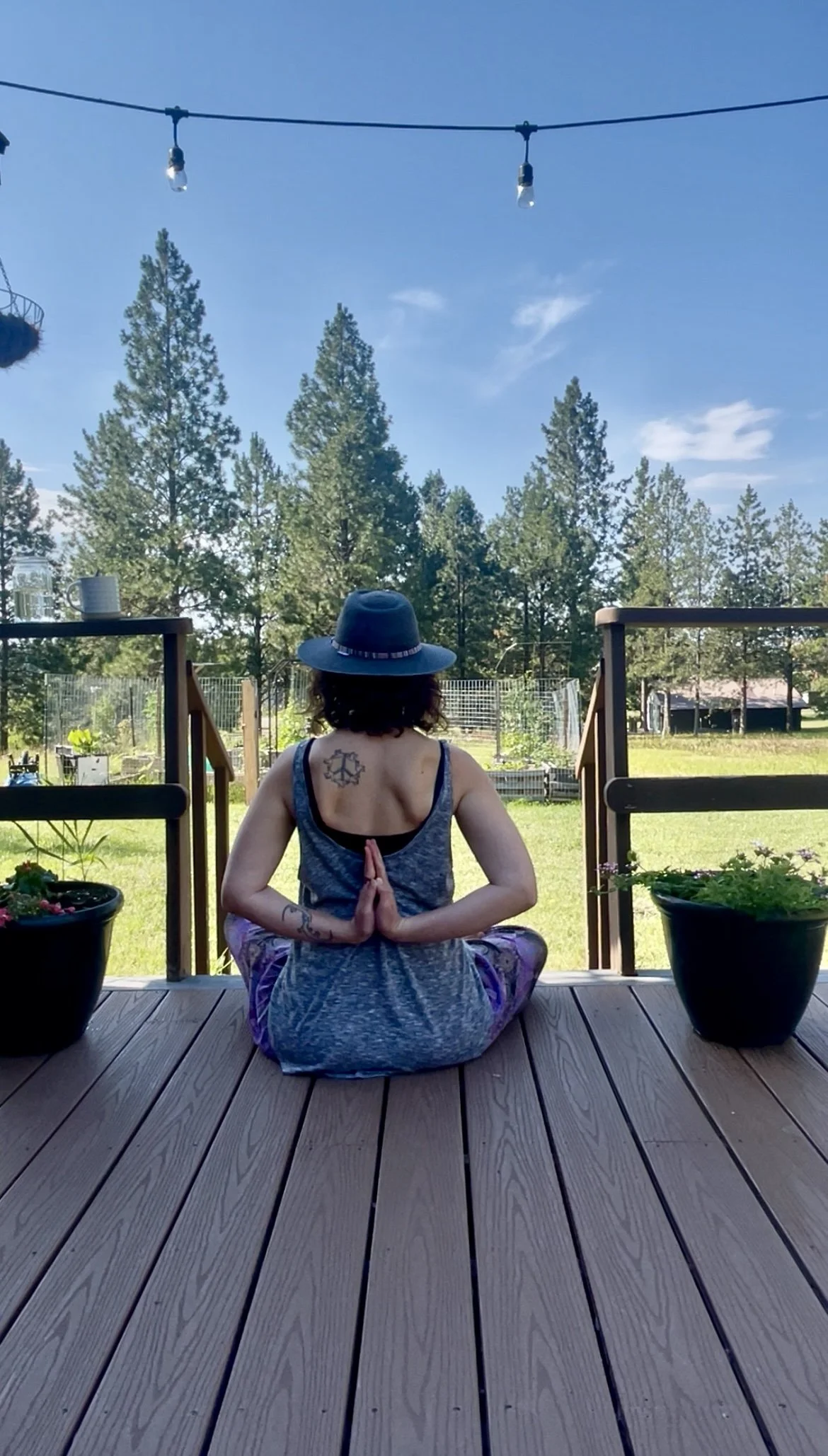 Photo of Kelsey Holmes sitting in easy seat with her back to the camera gazing out at her garden with her hands in prayer behind her back.