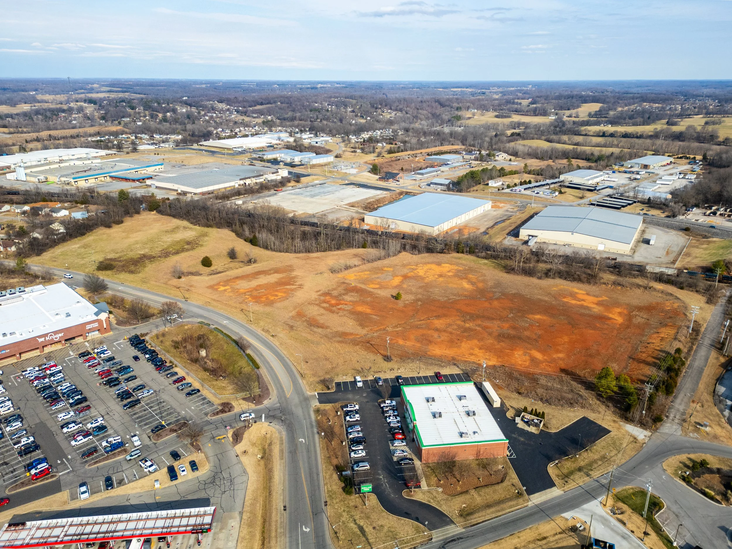 Aerial view of commercial and industrial buildings with a vacant lot and parking lot in a suburban area.