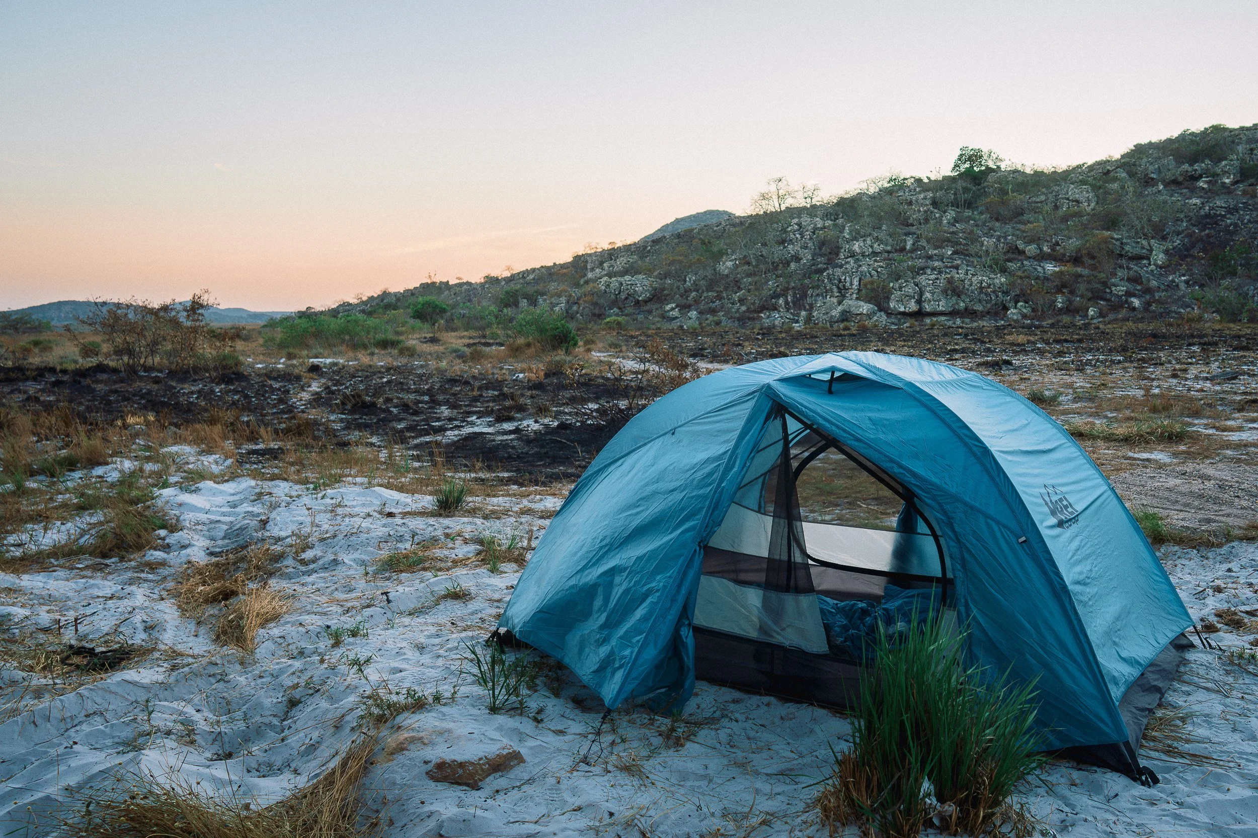A blue dome tent on pale sandy ground near Leandro’s rock shelter in Campos Tristes as evening falls.