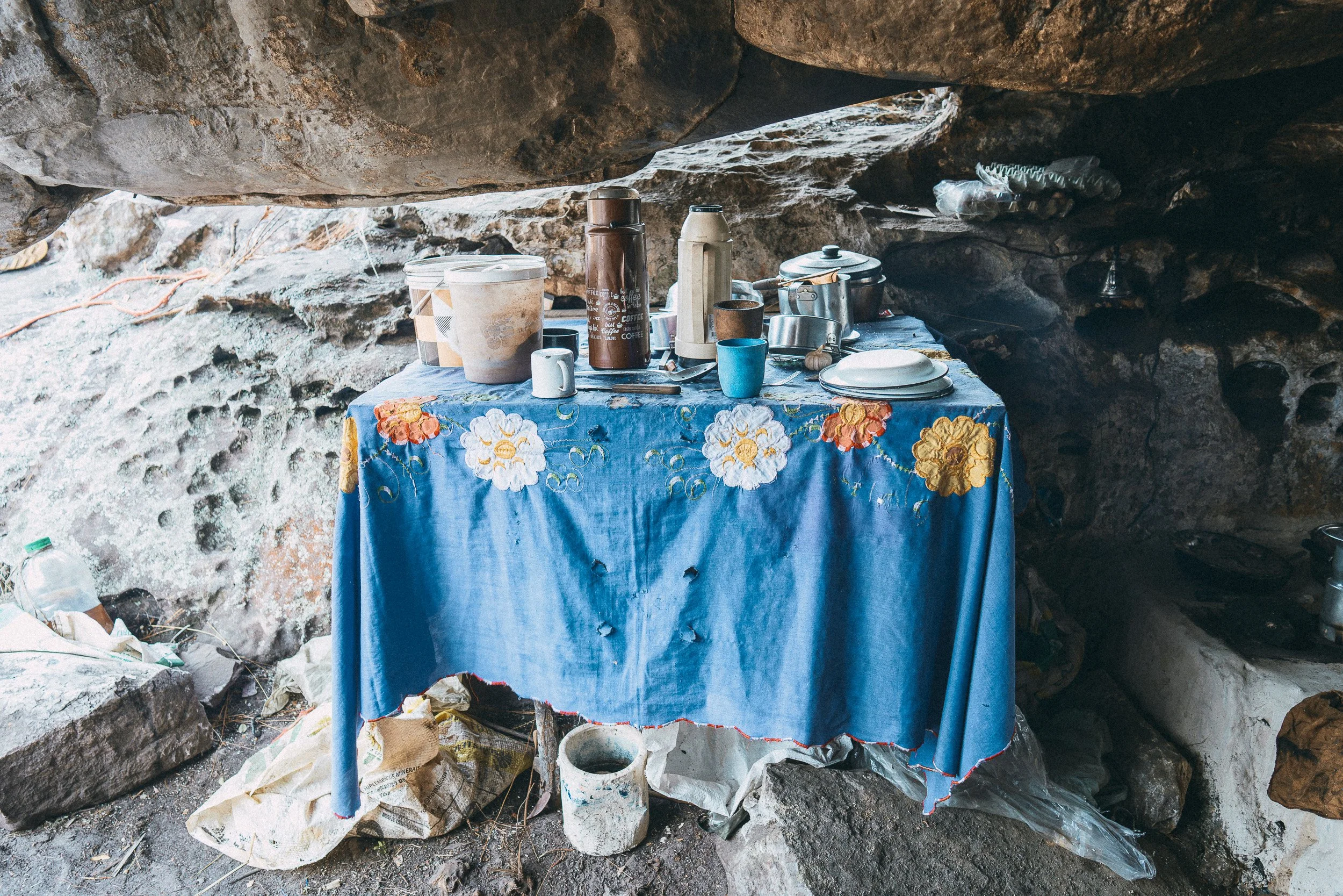 Pots, cups, and thermoses arranged on a table with a blue floral cloth beneath Leandro’s rock shelter in Campos Tristes.