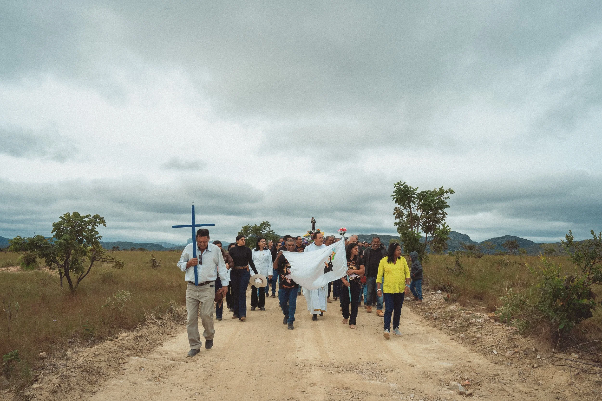 A crowd carrying a cross walks down a dirt road during the annual procession in Santa Rita, Serra do Espinhaço