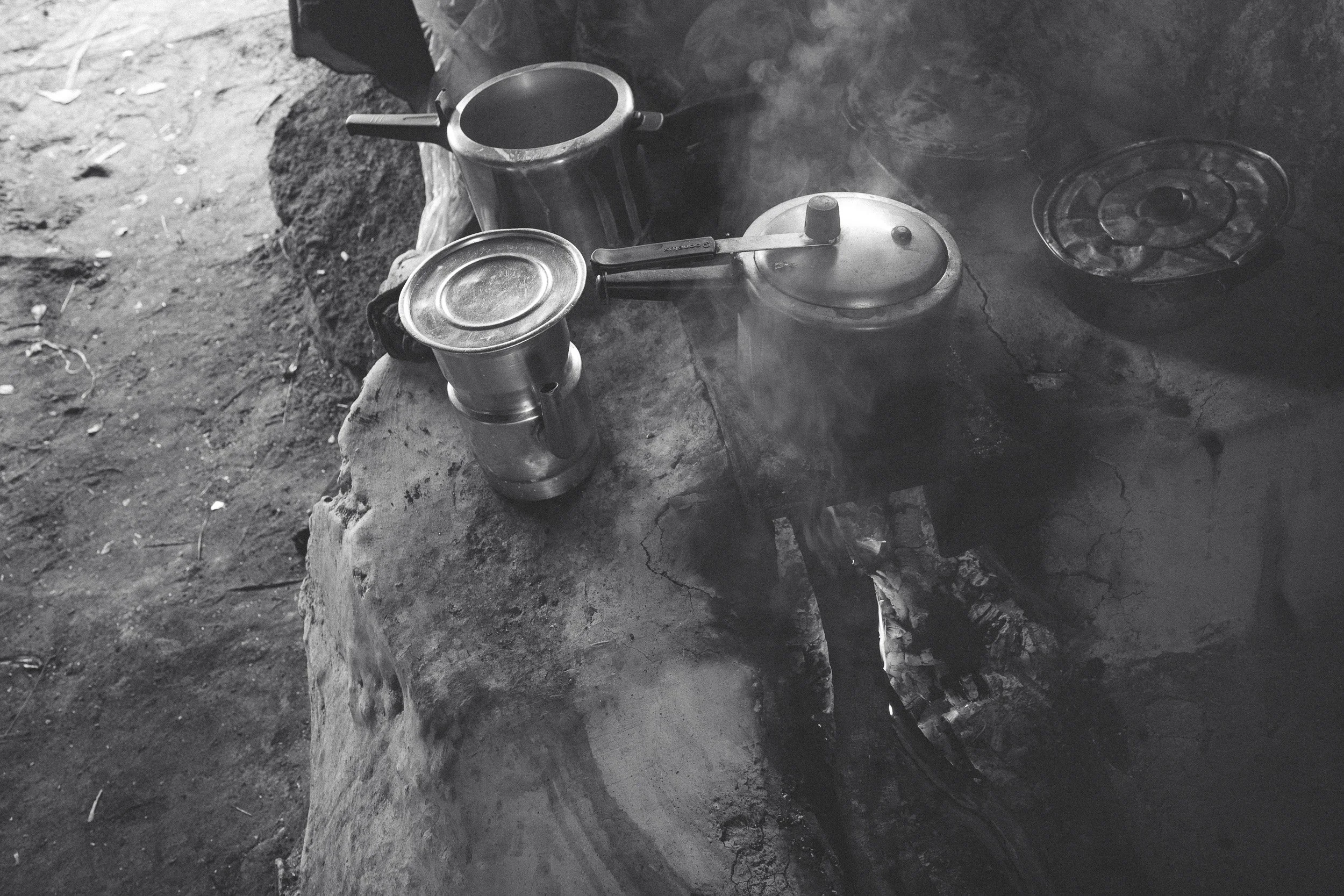 Black-and-white close-up of metal kettles and steaming pots on a wood-fired stone stove at Leandro’s shelter in Campos Tristes.