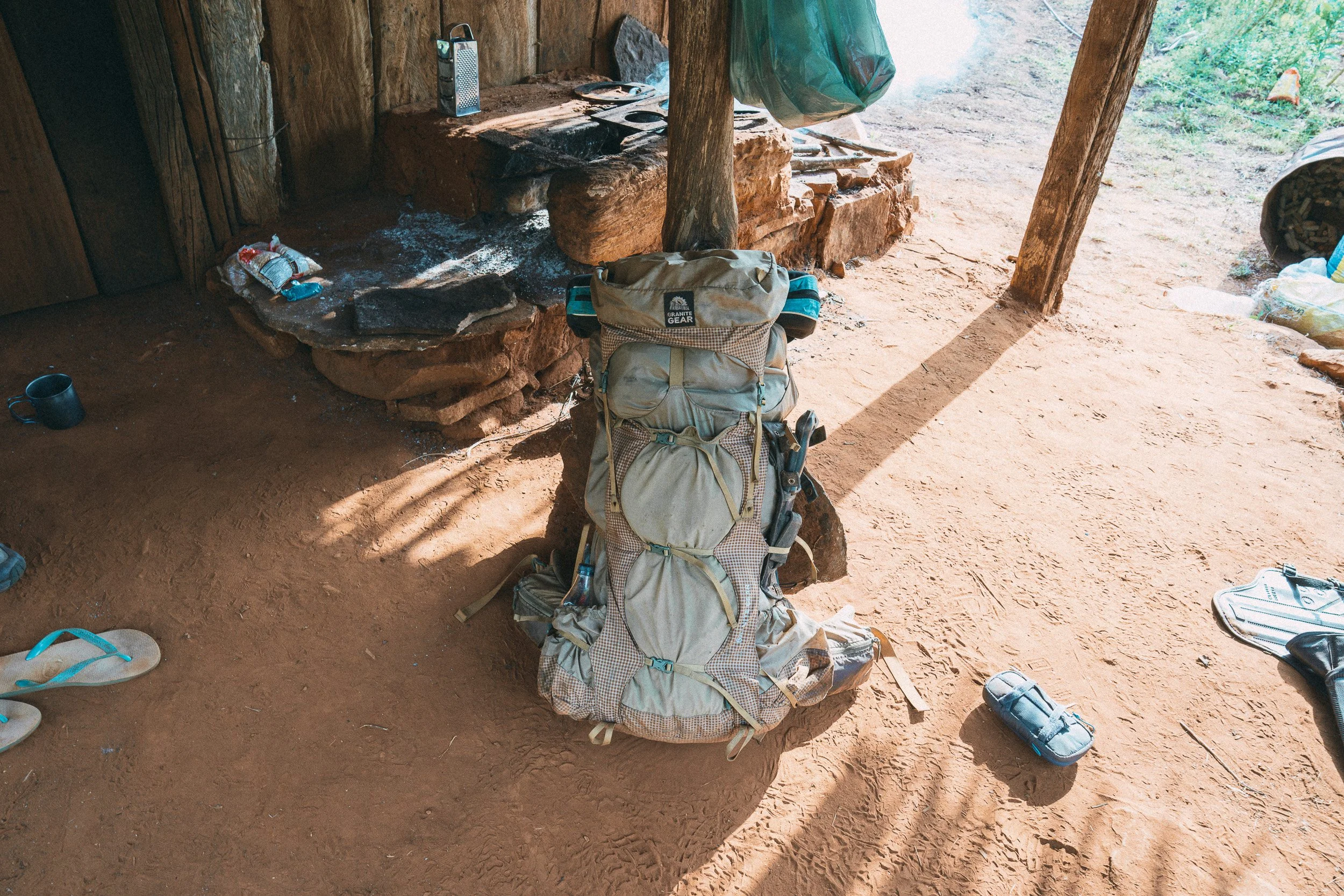 Eddie’s heavily loaded trekking backpack stands on the earthen floor beside a rustic stone cooking area in Folheta, Sempre Vivas National Park