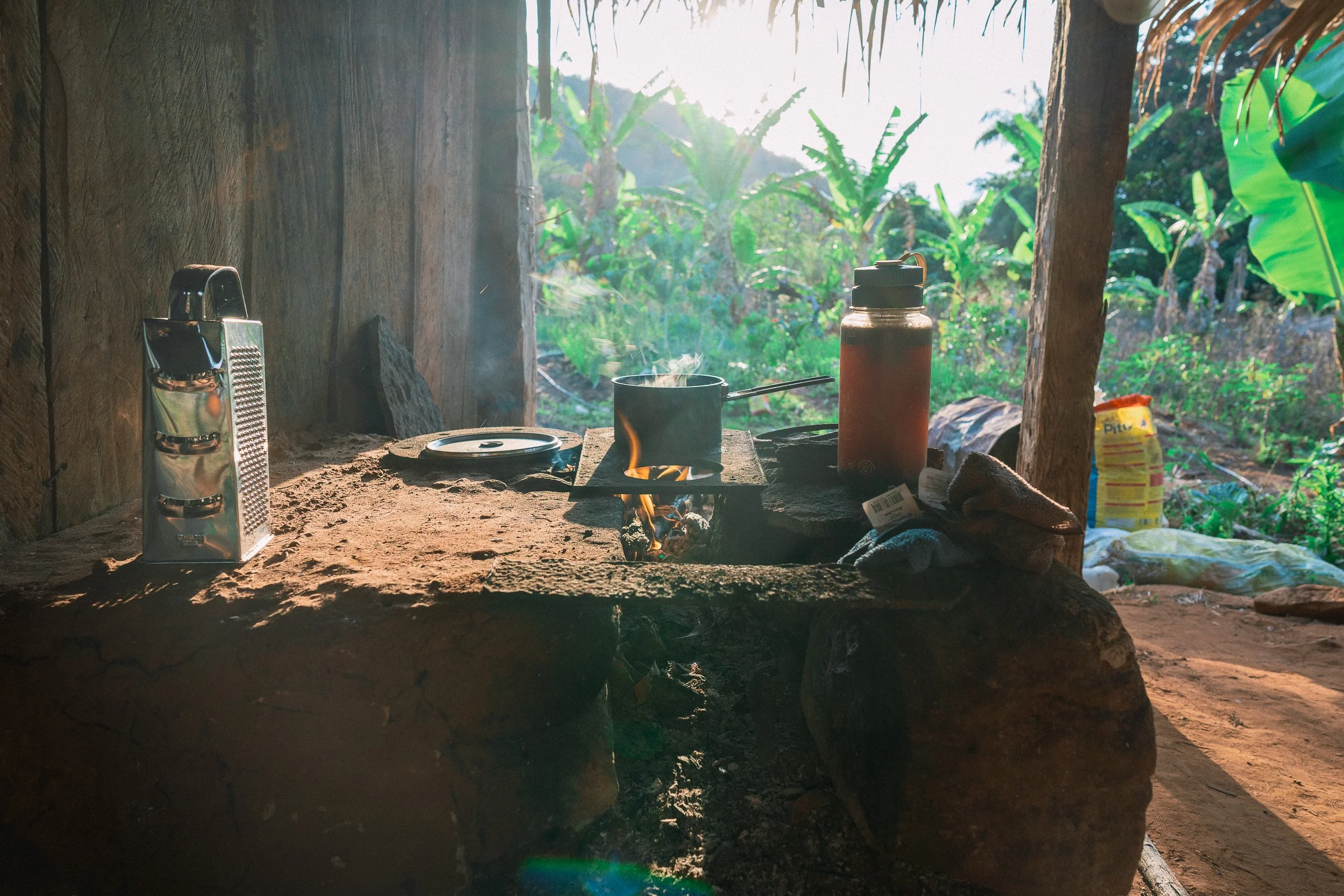 A pot heats over a wood fire on a rustic stone stove, with a grater and thermos alongside, at Folheta in Sempre Vivas National Park