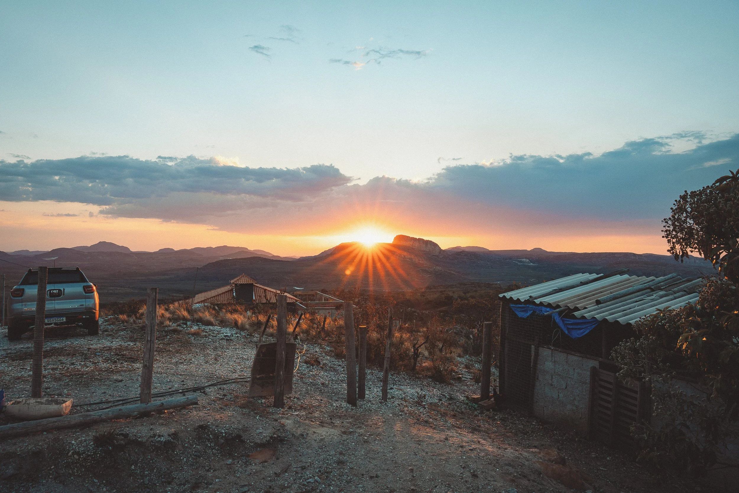 Sunset over Tromba d’Anta mountain, seen from Branquinho’s porch near Guinda, Diamantina, with a gate and farm buildings in the foreground.