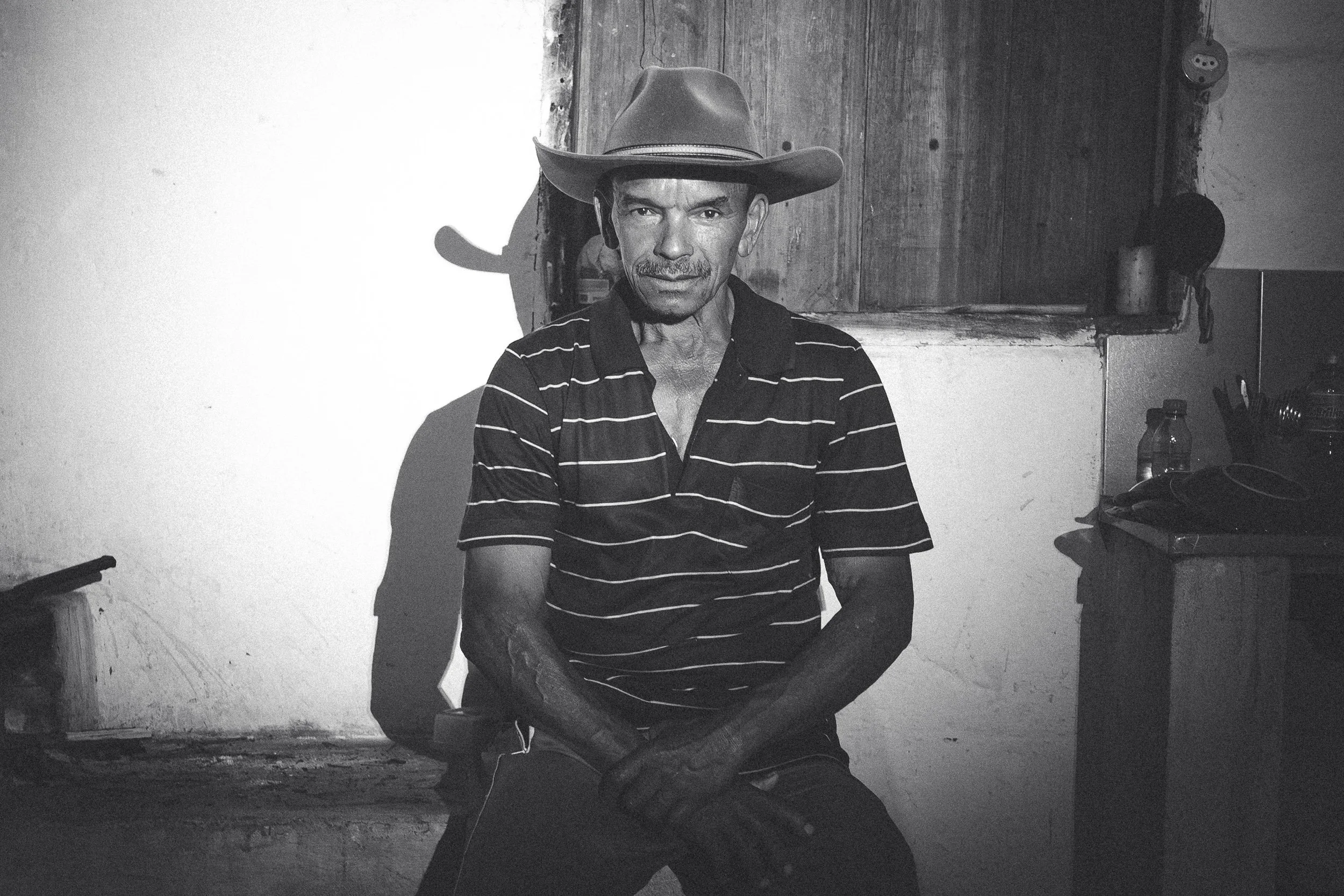 A black and white portrait of Santo sitting on the wood-fired stove at Mozart's house on the Chapada do Couto, Rio Preto State Park