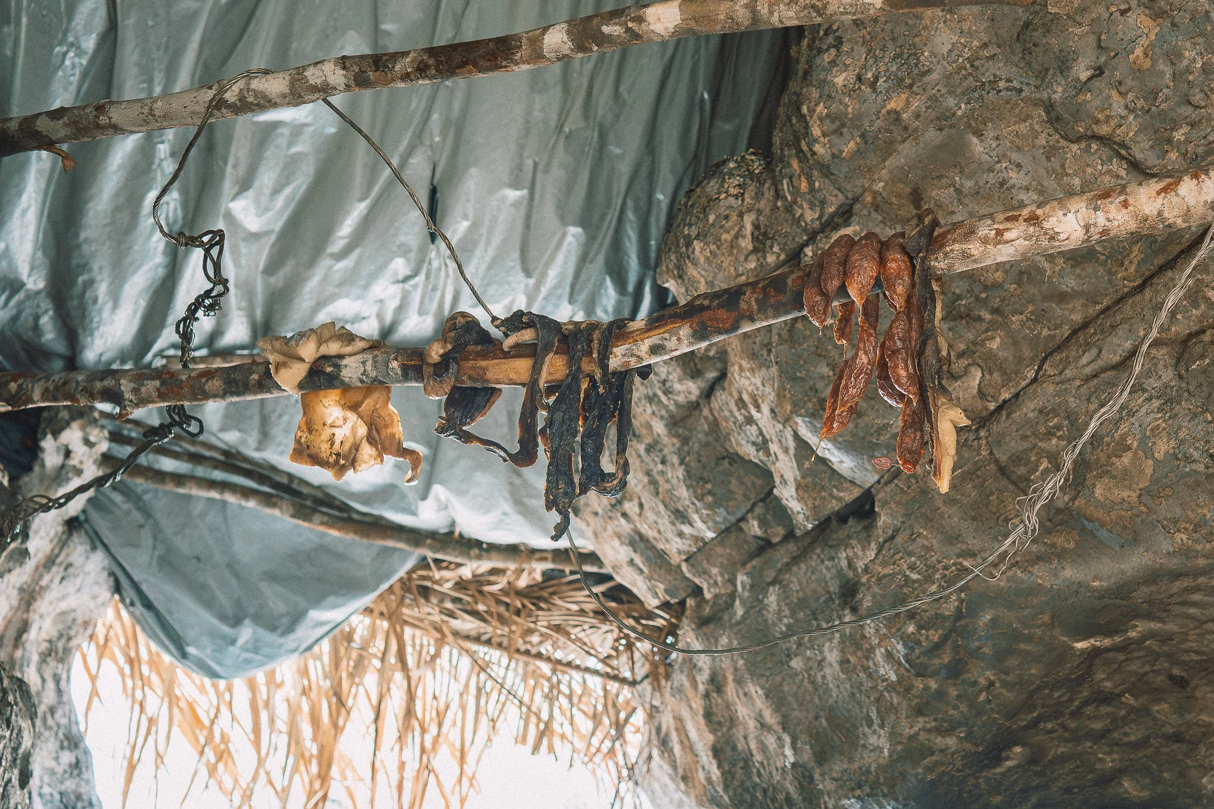 An assortment of dried meats and sausages hang on a branch between rock walls inside Leandro’s rock shelter at Campos Tristes in Sempre Vivas National Park.