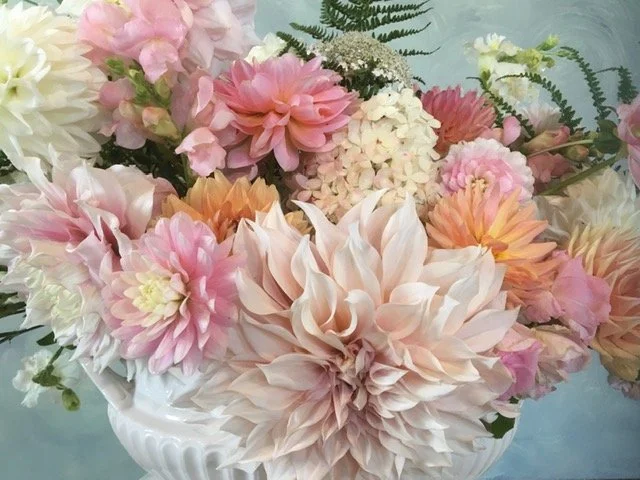 A white ceramic vase filled with pink, peach, white, and cream-colored flowers, including dahlias, hydrangeas, and ferns.