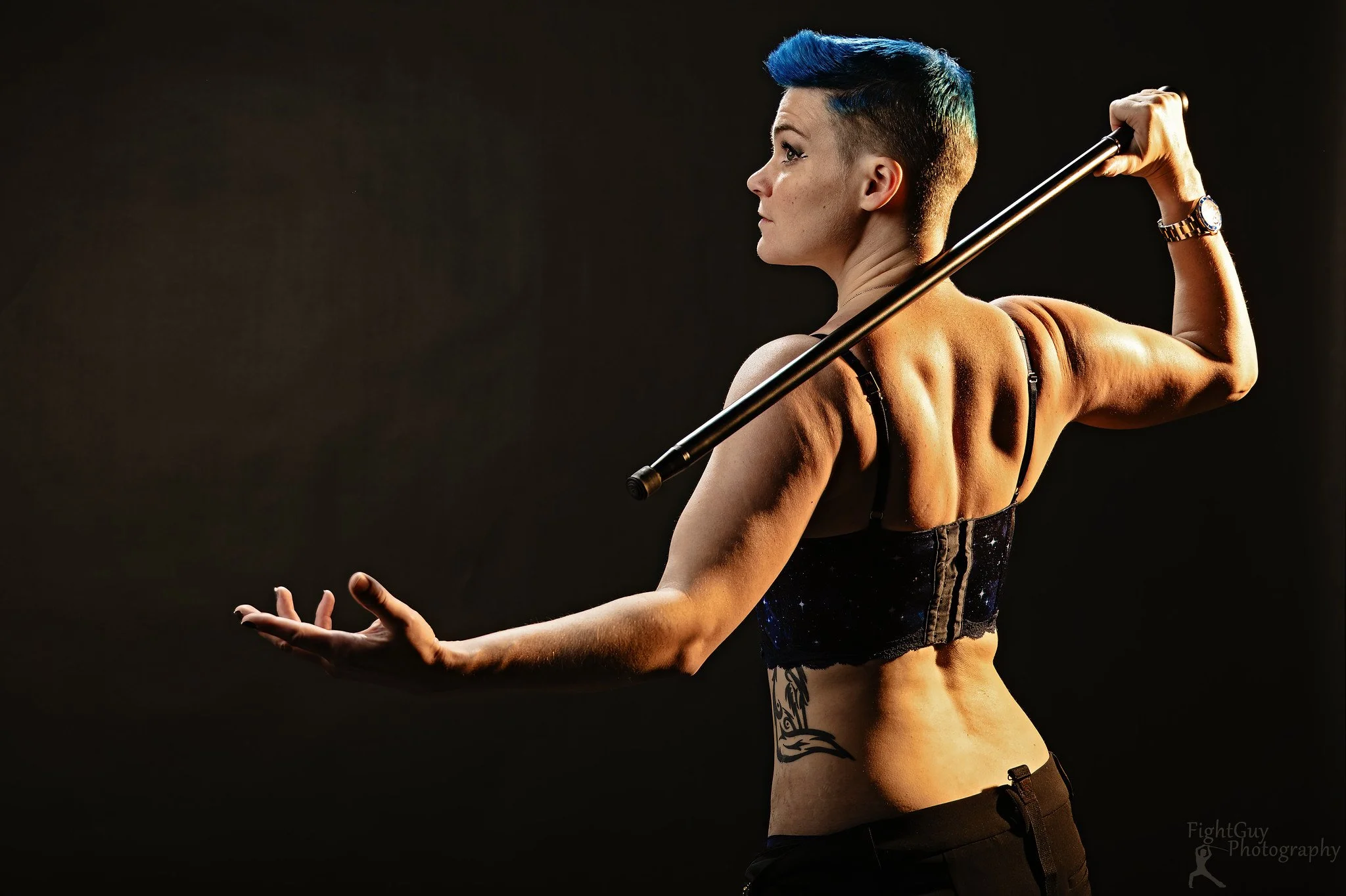 A muscular woman with short blue hair poses for an art glamour photo in the studio