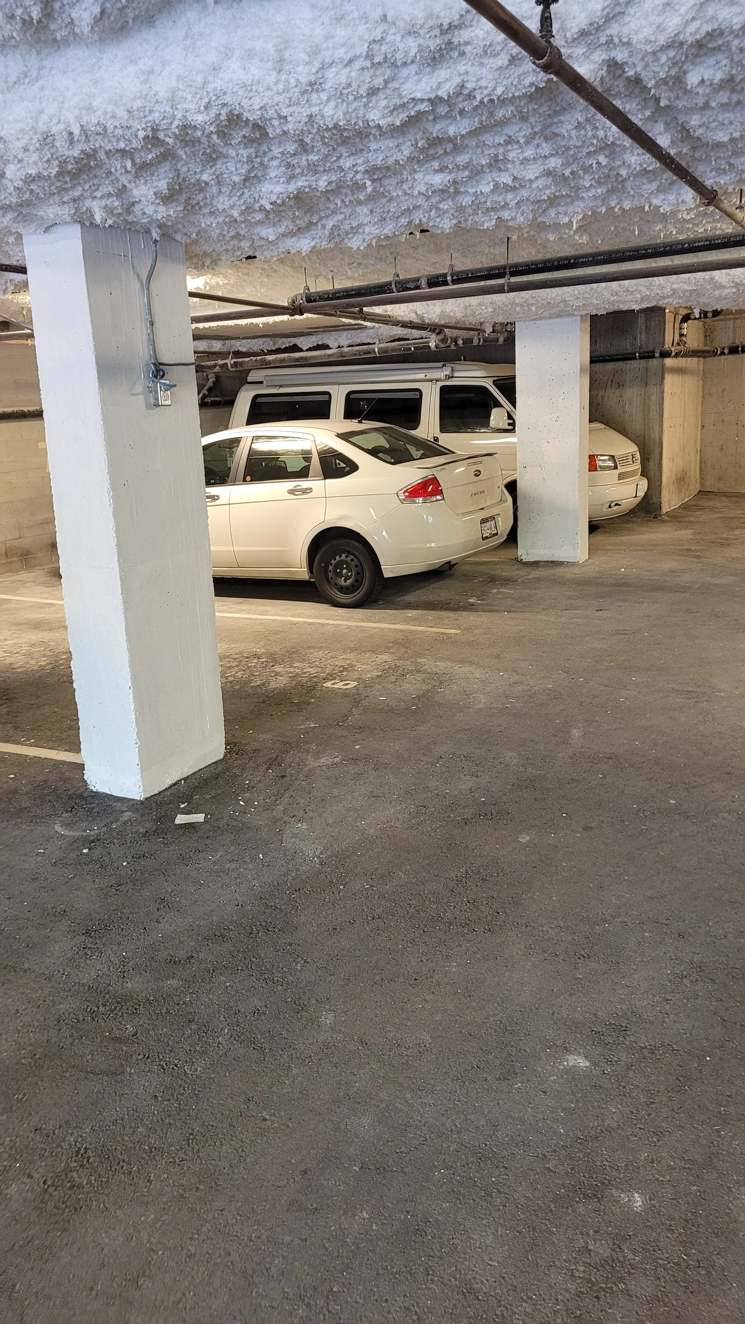 Indoor parking garage with three parked vehicles and concrete support pillars.