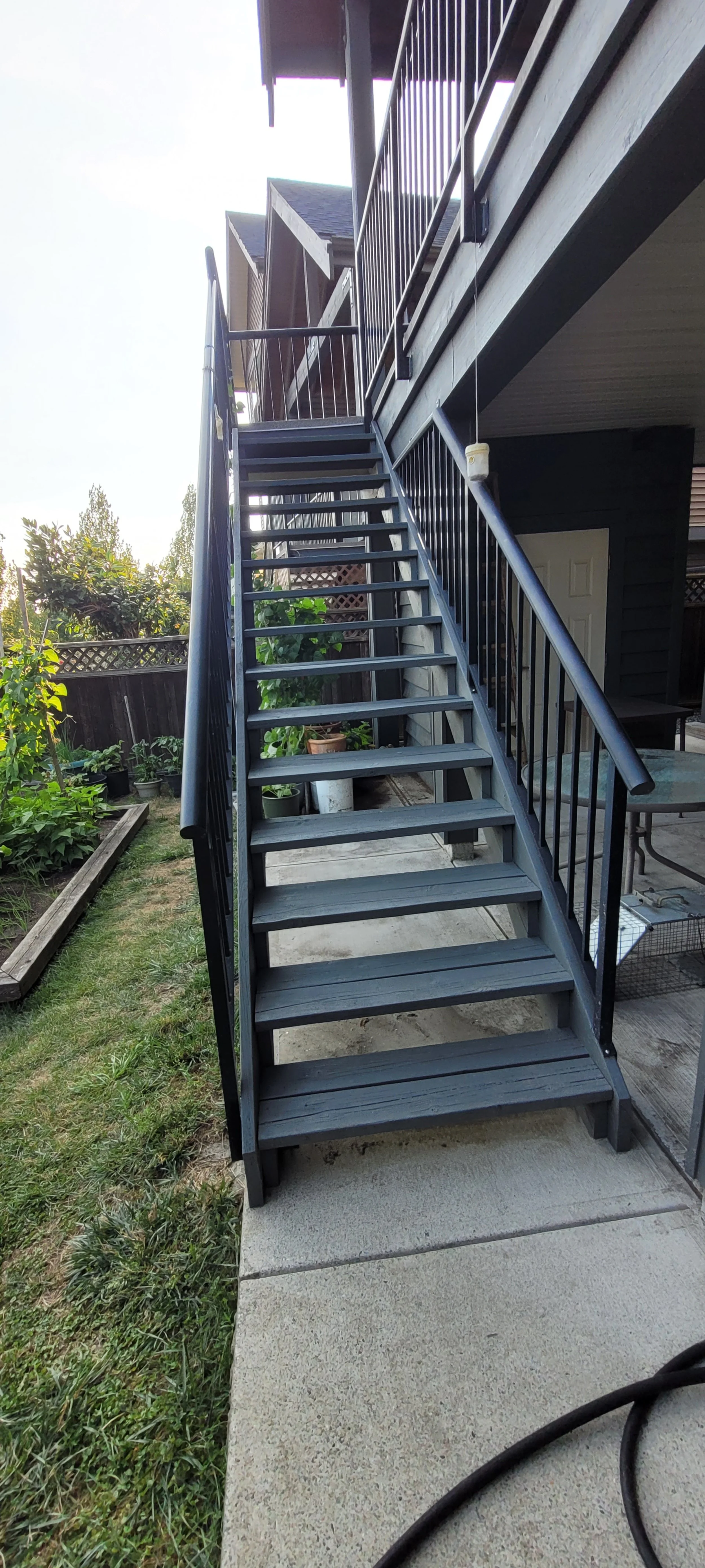 Exterior of a house with a black staircase leading up to a second-floor balcony, with a garden on the left side.