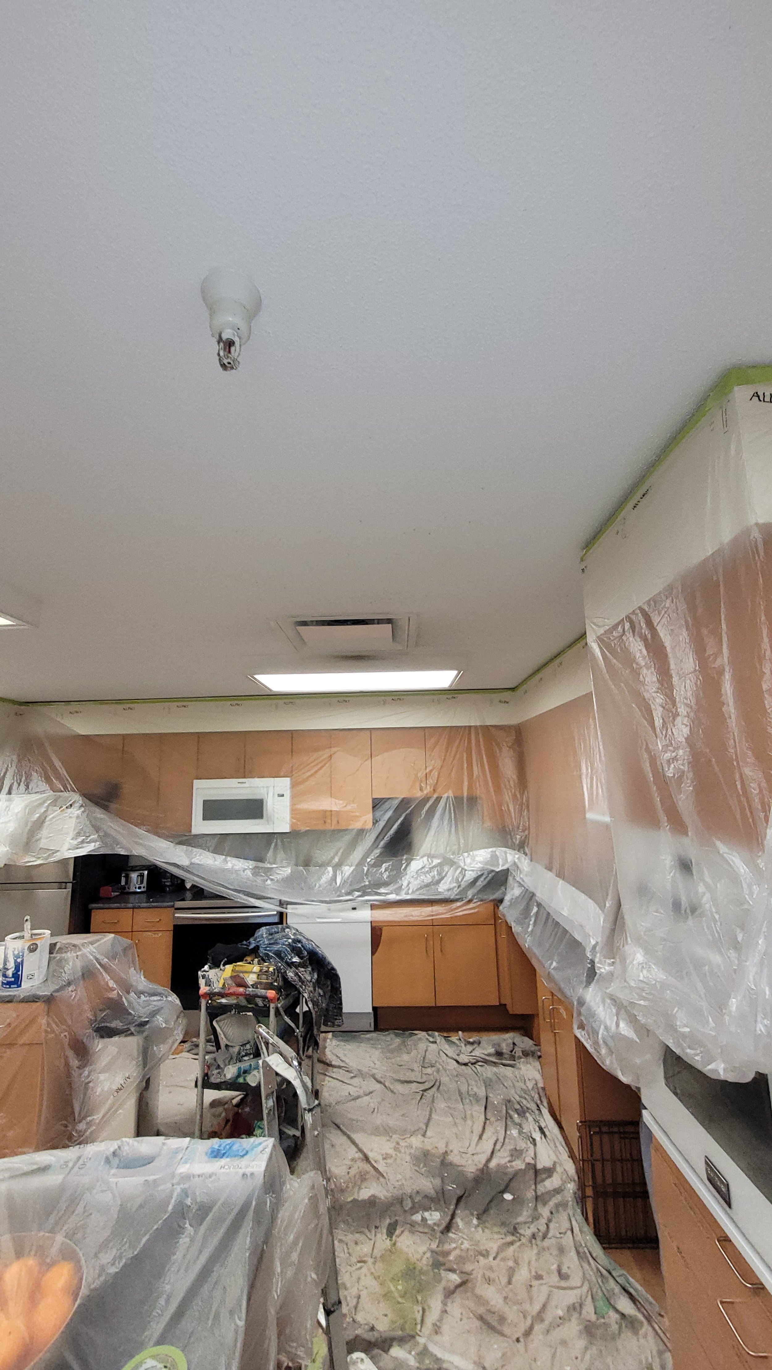 Kitchen area undergoing renovation, covered with plastic sheets, a ladder, and construction tools and supplies.