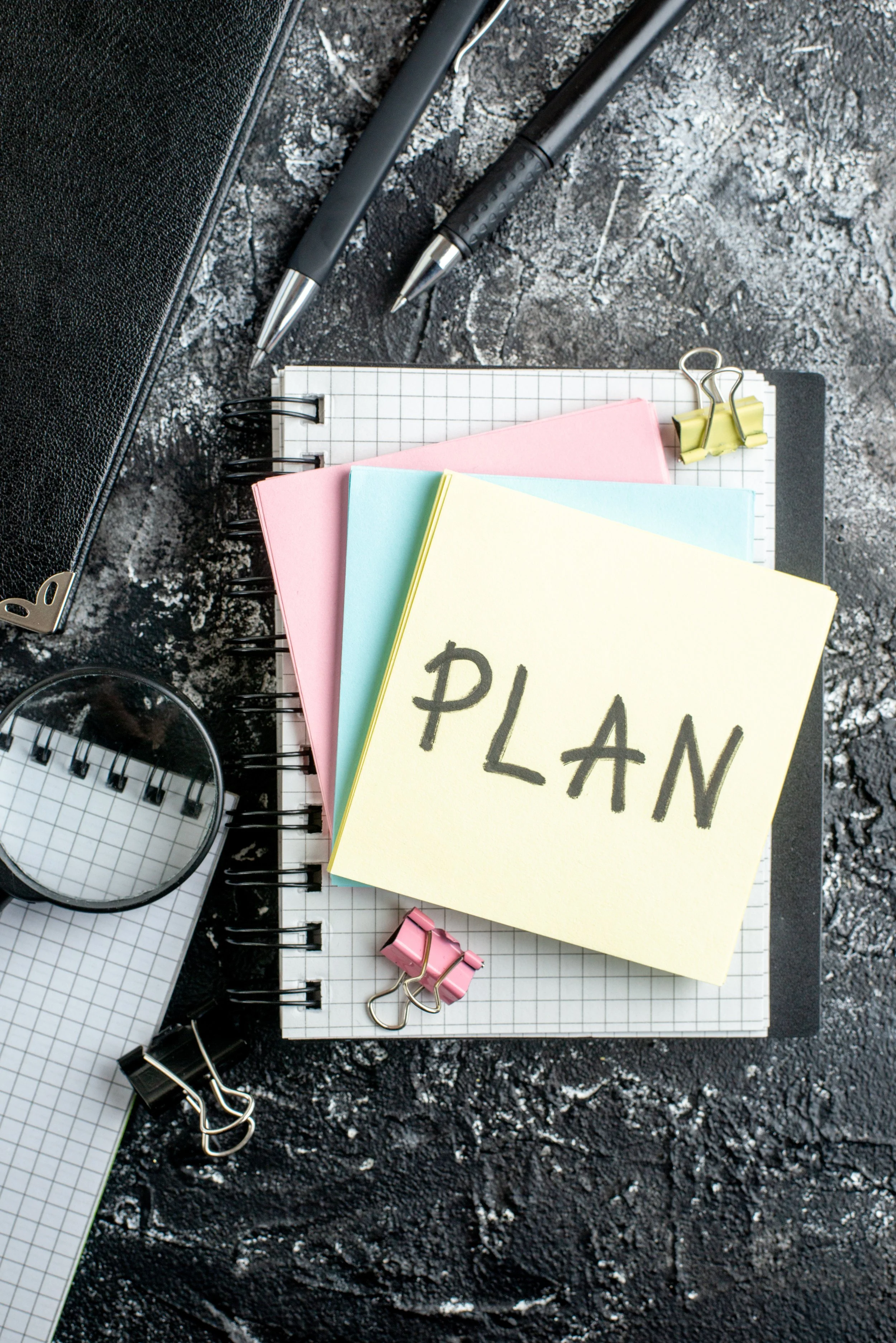 Top view photo of sticky notes stacked on top of a notebook. The word "Plan" is written on the top sticky note.