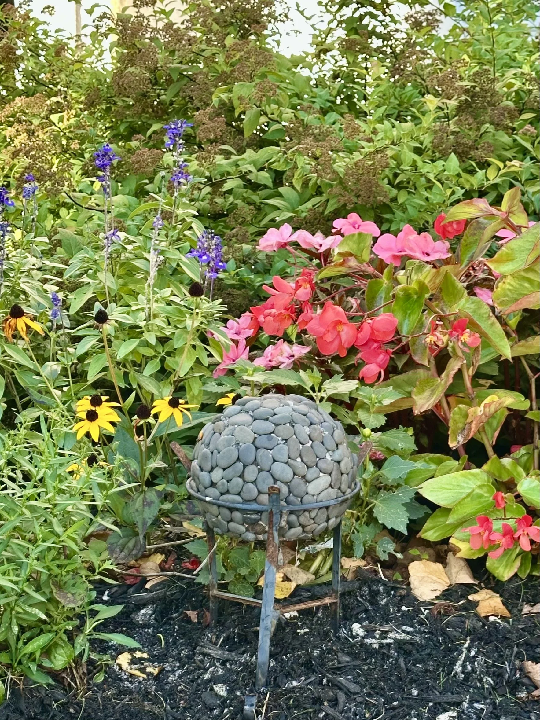 A Stone Sphere nestled among flowers in a garden