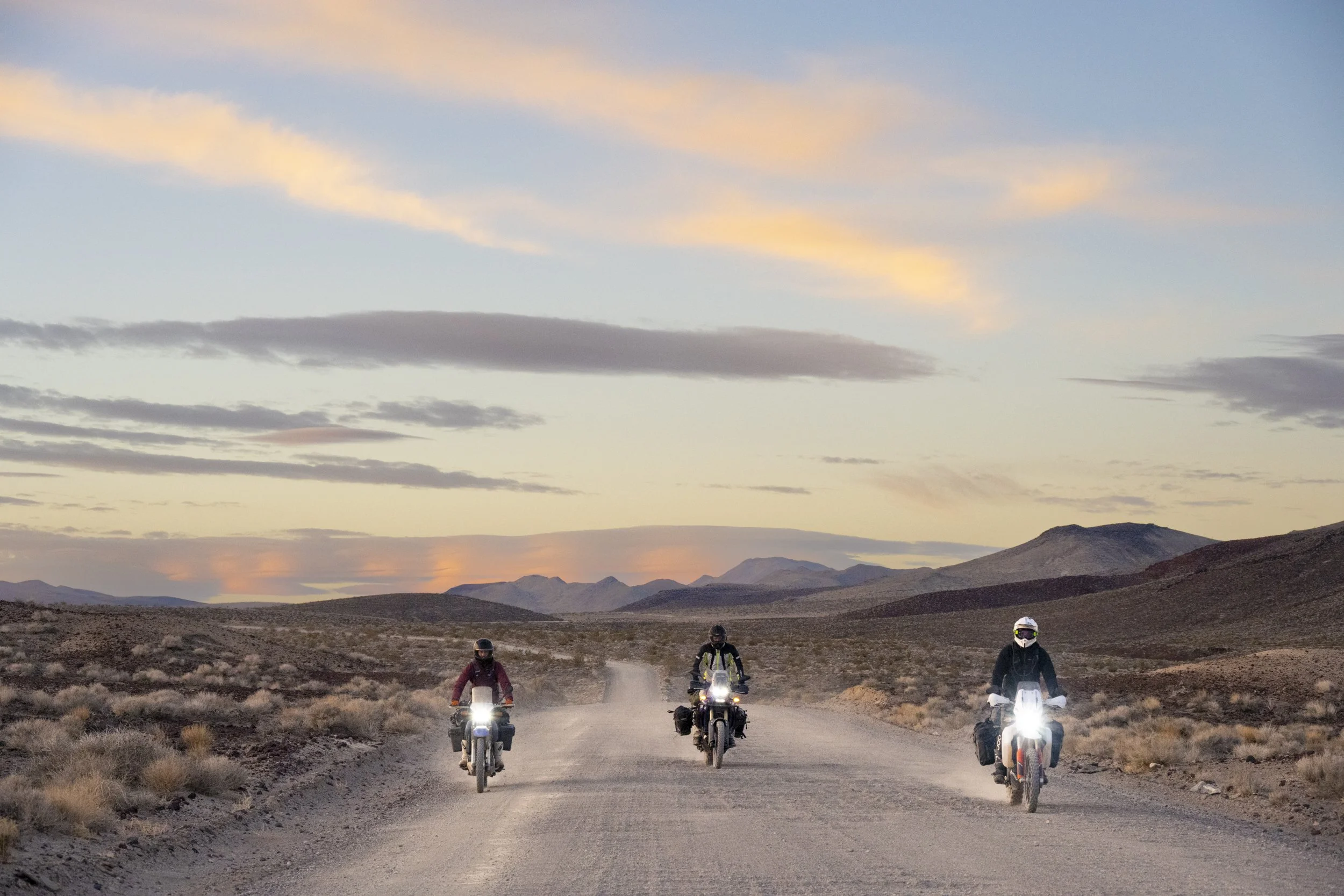 Three motorcycle riders on a dirt road  with the sun setting behind them in the desert from death valley