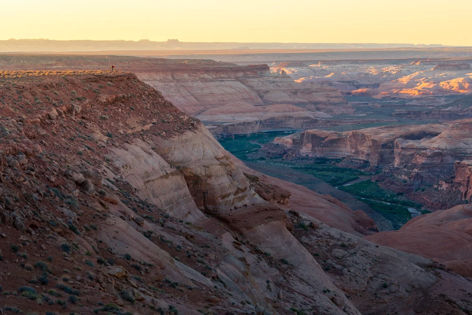Man standing on cliff edge above river, taking picture in canyons of utah