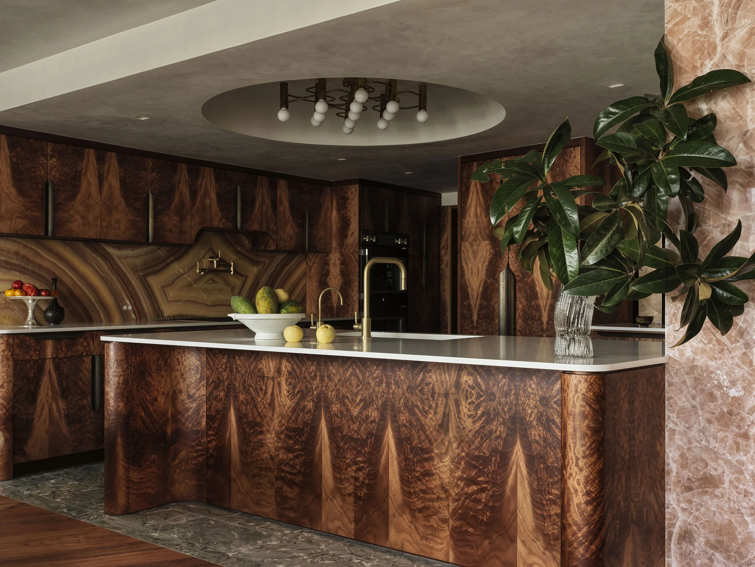 A kitchen featuring a curved island and cabinets okoume veneers, a vibrant onyx backsplash, and a domed ceiling with a vintage brass light fixture