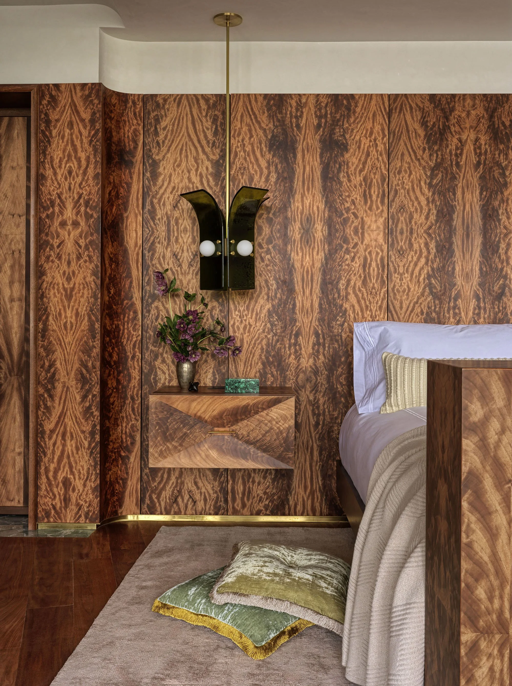 A bedroom featuring an Okoume wall, a matching floating nightstand with a marquetry front, and a green glass palm-shaped pendant
