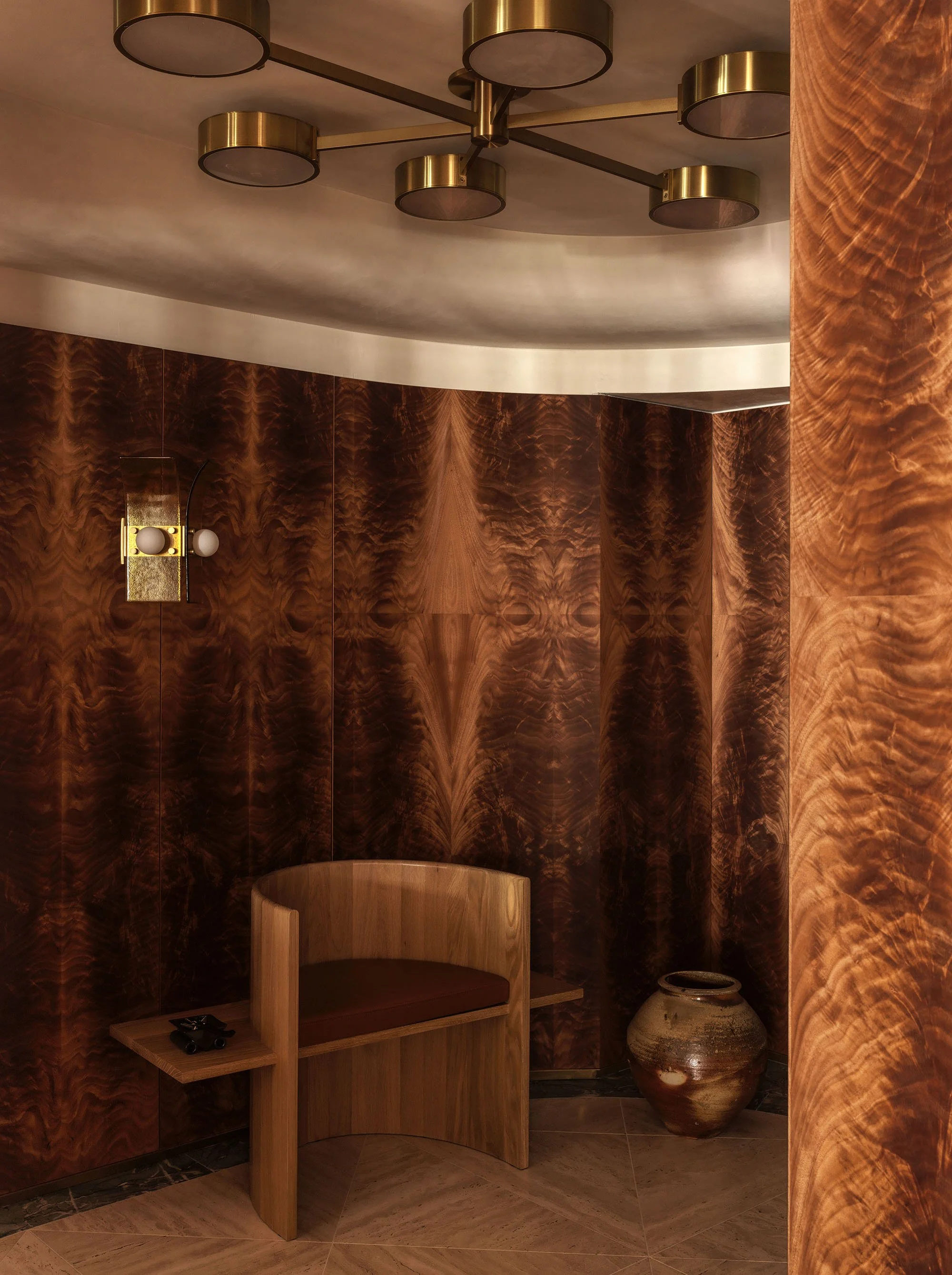 An entry foyer featuring a curved bench with integral shelves and an Anagama kiln vessel in front of a curving okoume veneer wall
