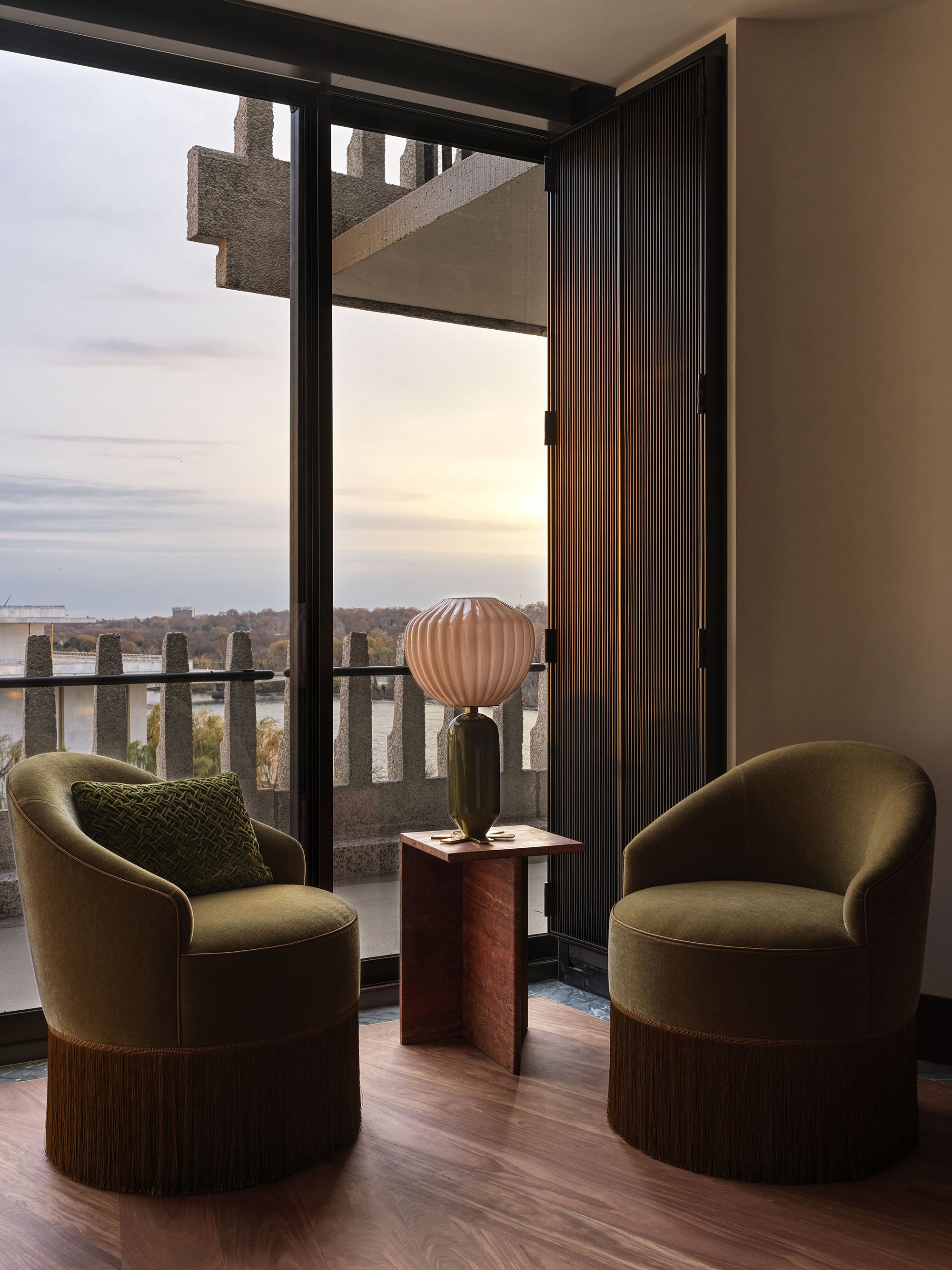 A sitting nook in the Watergate with fringed chairs looking through a concrete balcony to the Potomac River