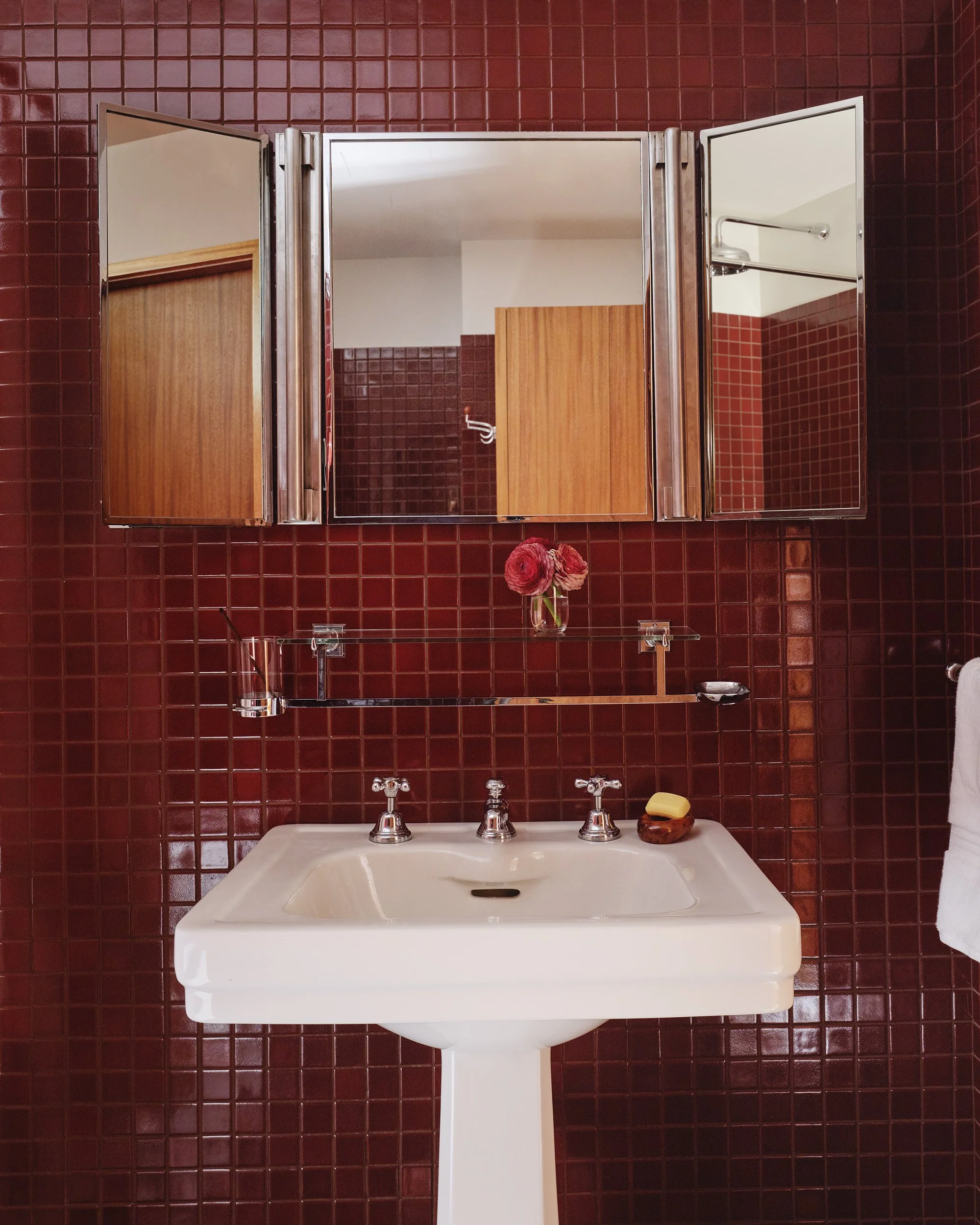 A bathroom in the Rockefeller Apartments with red Heath Ceramics tiles and a antique pedestal sink