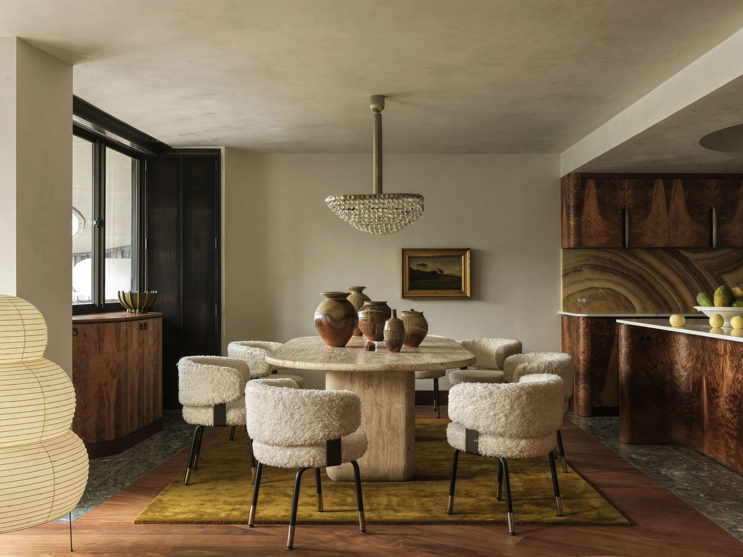 A dining room featuring an oval travertine table, vintage sheepskin chairs, and a 1960s Viennese chandelier
