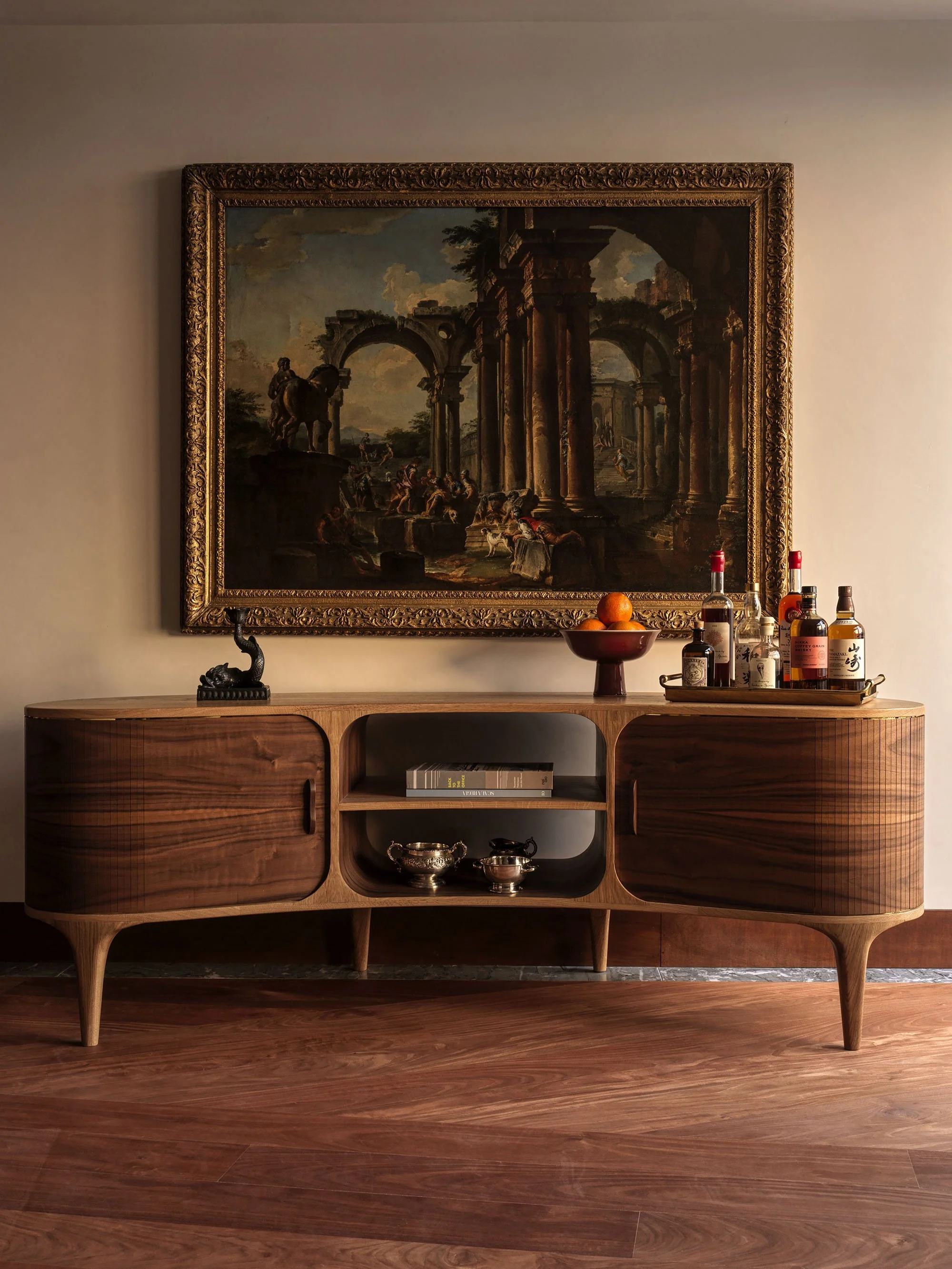 A vignette featuring a sculptural walnut credenza and a richly framed 1730 Capriccio of Roman Ruins with Figures by Giovanni Paolo Panini