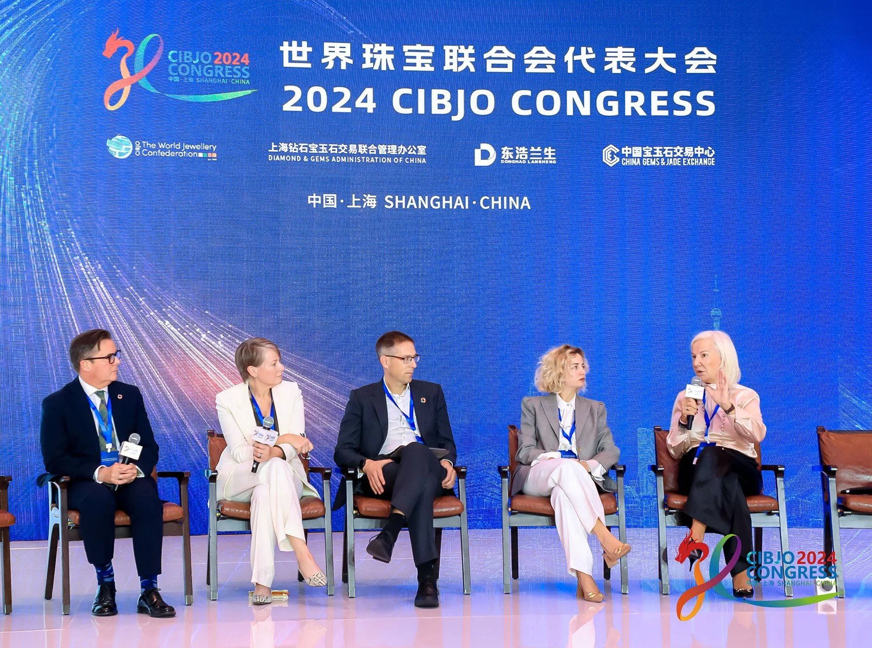 Panel discussion at the 2024 CIBJO Congress held in Shanghai, China. Five individuals seated on stage, some holding microphones, with a large blue screen behind them displaying event details in English and Chinese, including the event name and sponsors.