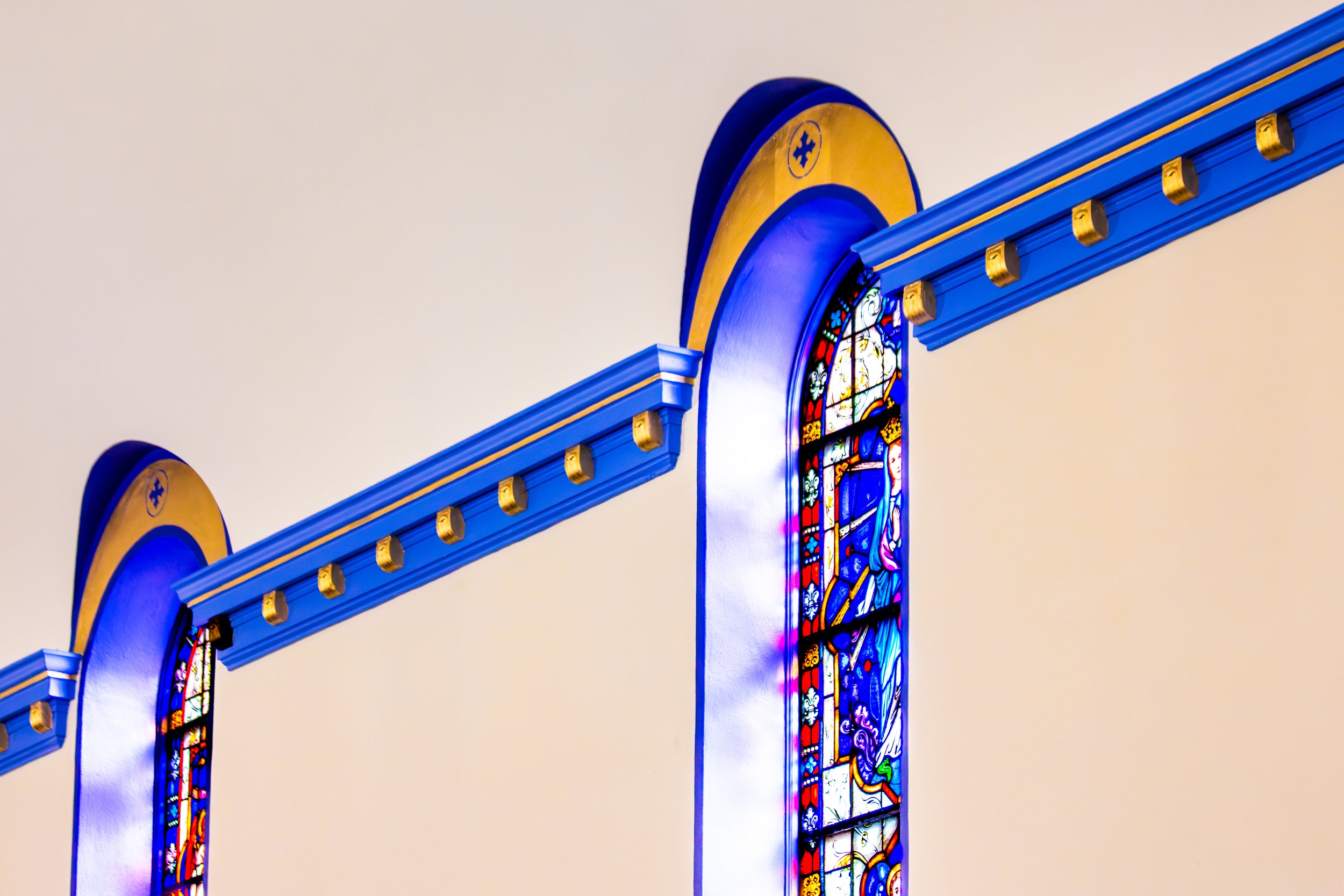 Colorful stained glass windows in a church, framed by blue and gold architectural details.