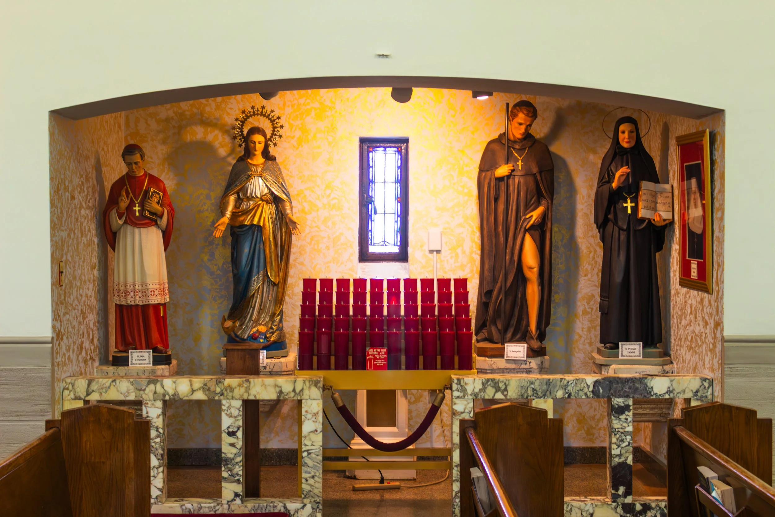 Religious statues displayed in a church chapel with candles in front.