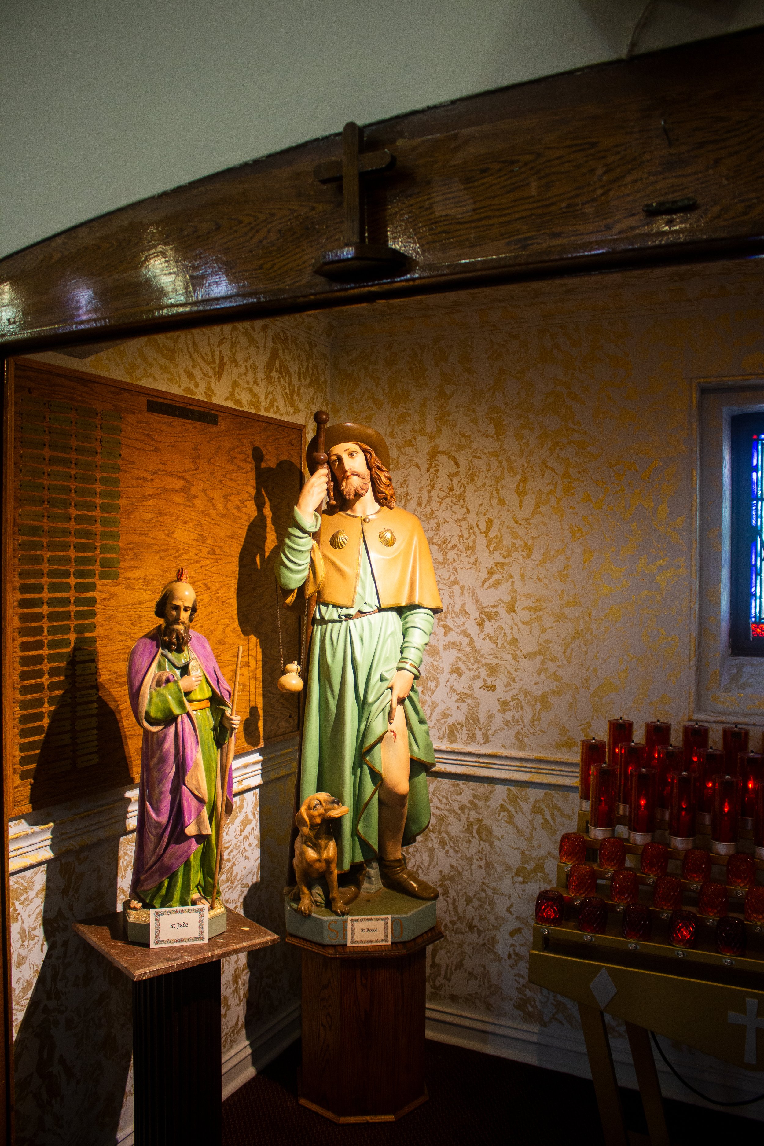 Religious statues of St. Jude and St. Rocco with a dog, displayed in a room with candles.
